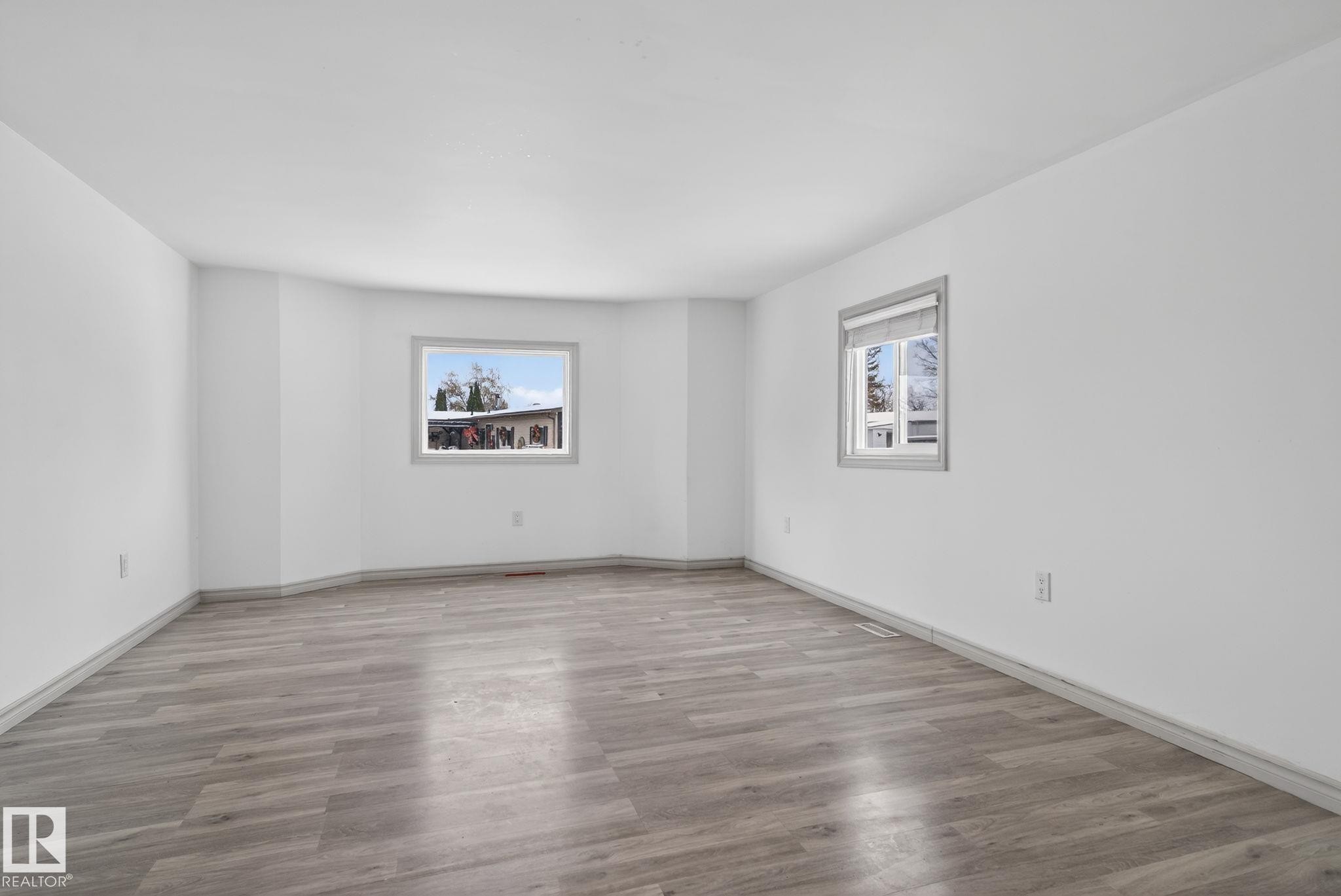 Spacious room featuring light wood-finish flooring, crisp white walls, and two windows with grey trim providing natural illumination - 543 Evergreen Park Northwest, Edmonton, AB - Indoor