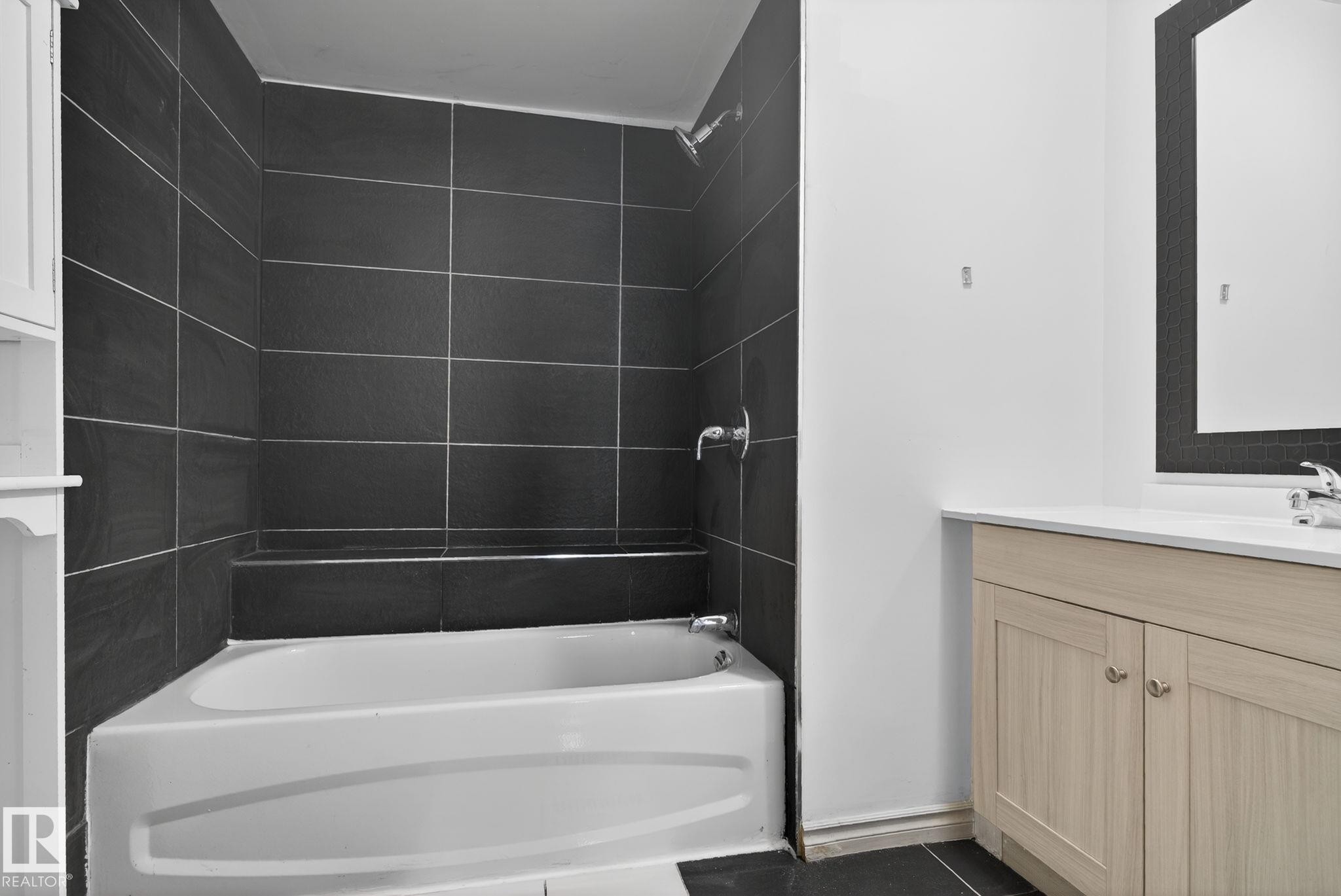 Bathroom featuring a tiled shower with a built-in bench, a white bathtub, a wood-finish vanity with a white countertop, and a wall-mounted mirror - 543 Evergreen Park Northwest, Edmonton, AB - Indoor