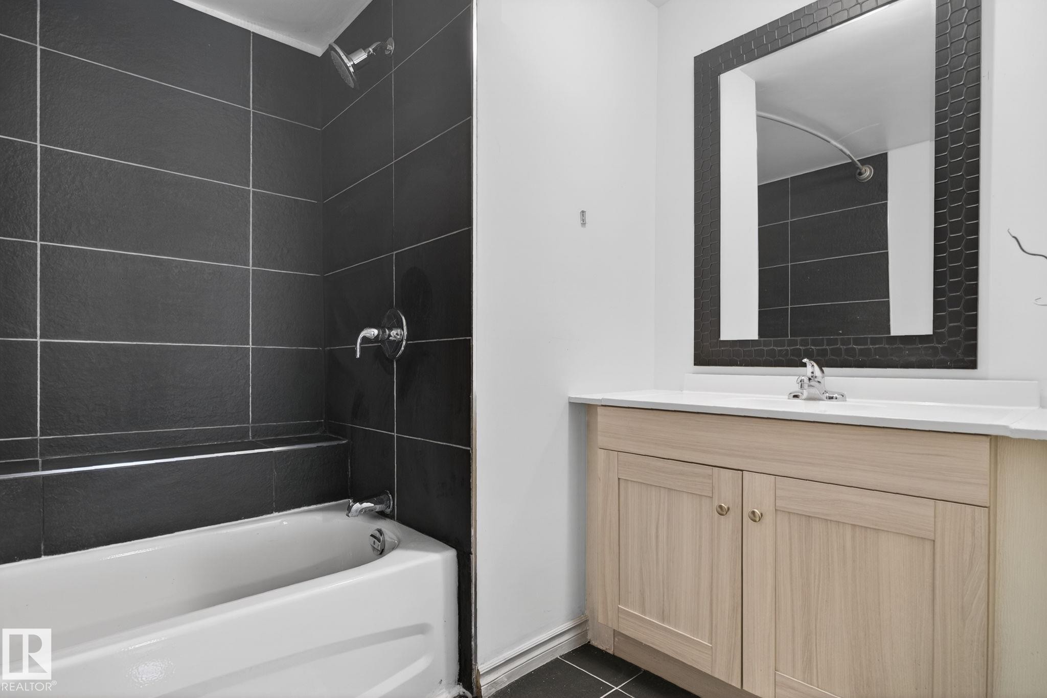 Bathroom featuring a tub/shower combination with dark tile surround, a light wood-finish vanity, white countertop, and a framed mirror - 543 Evergreen Park Northwest, Edmonton, AB - Indoor Photo Showing Bathroom