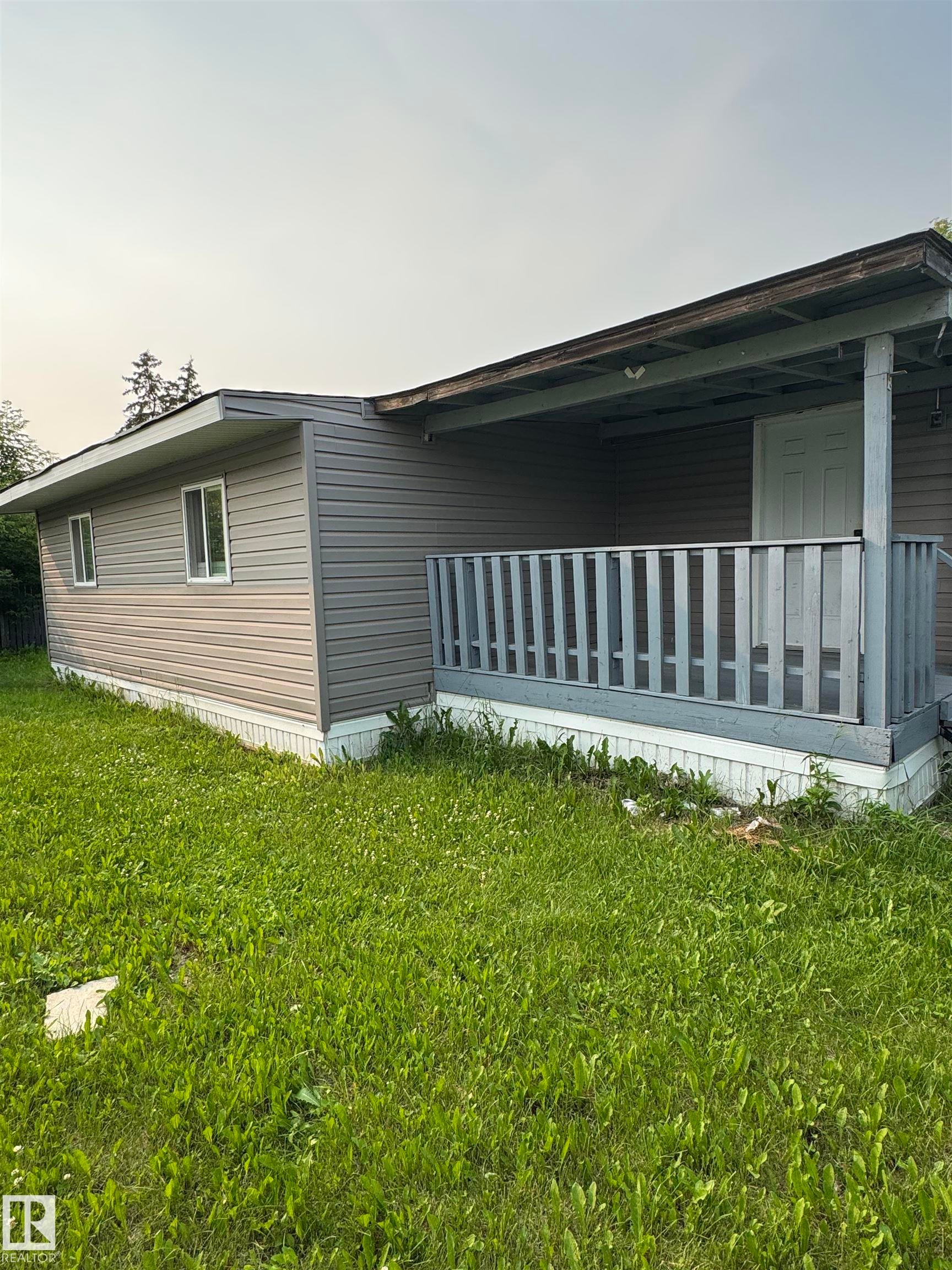 Property exterior featuring gray horizontal siding and a covered front porch with a wood railing - 543 Evergreen Park Northwest, Edmonton, AB - Outdoor