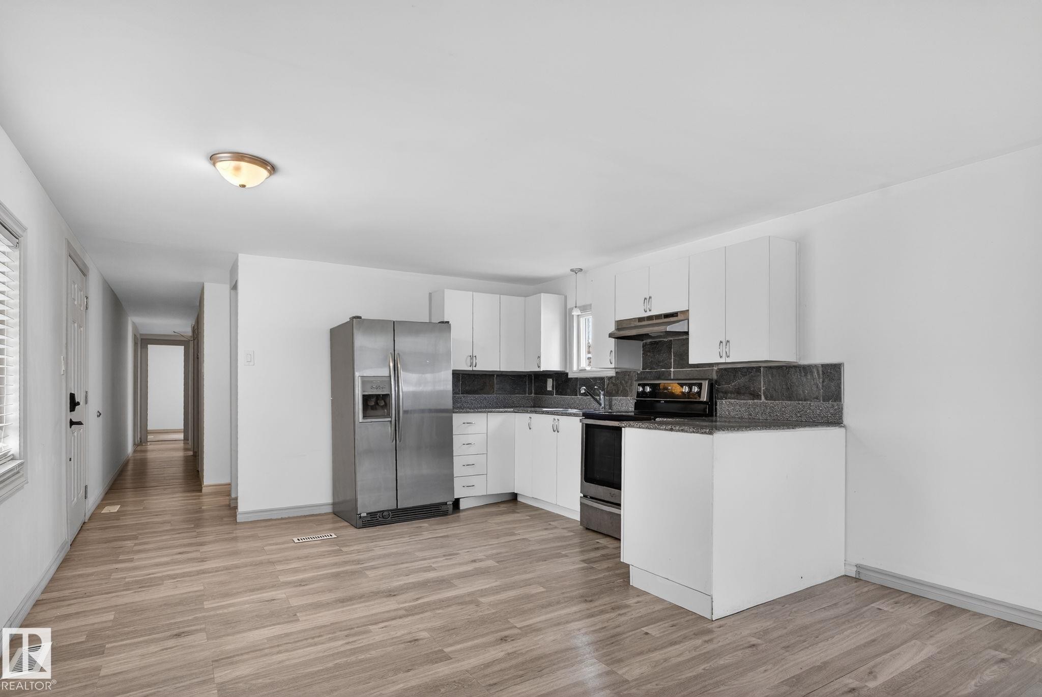 Kitchen featuring white cabinetry, dark stone countertops, stainless steel appliances, and wood-finish flooring - 543 Evergreen Park Northwest, Edmonton, AB - Indoor Photo Showing Kitchen