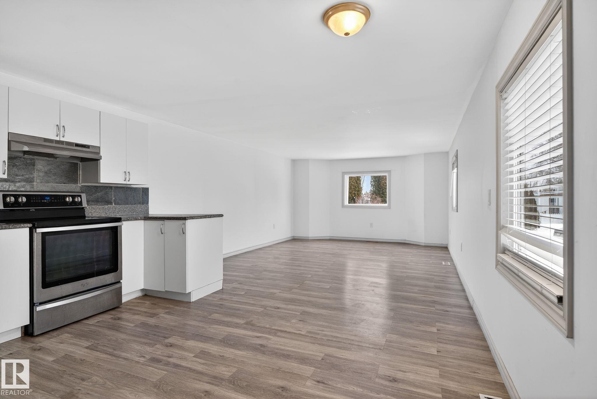 Open-concept living space featuring wood-finish flooring, white cabinetry with stainless steel hardware, and a stainless steel oven - 543 Evergreen Park Northwest, Edmonton, AB - Indoor Photo Showing Kitchen