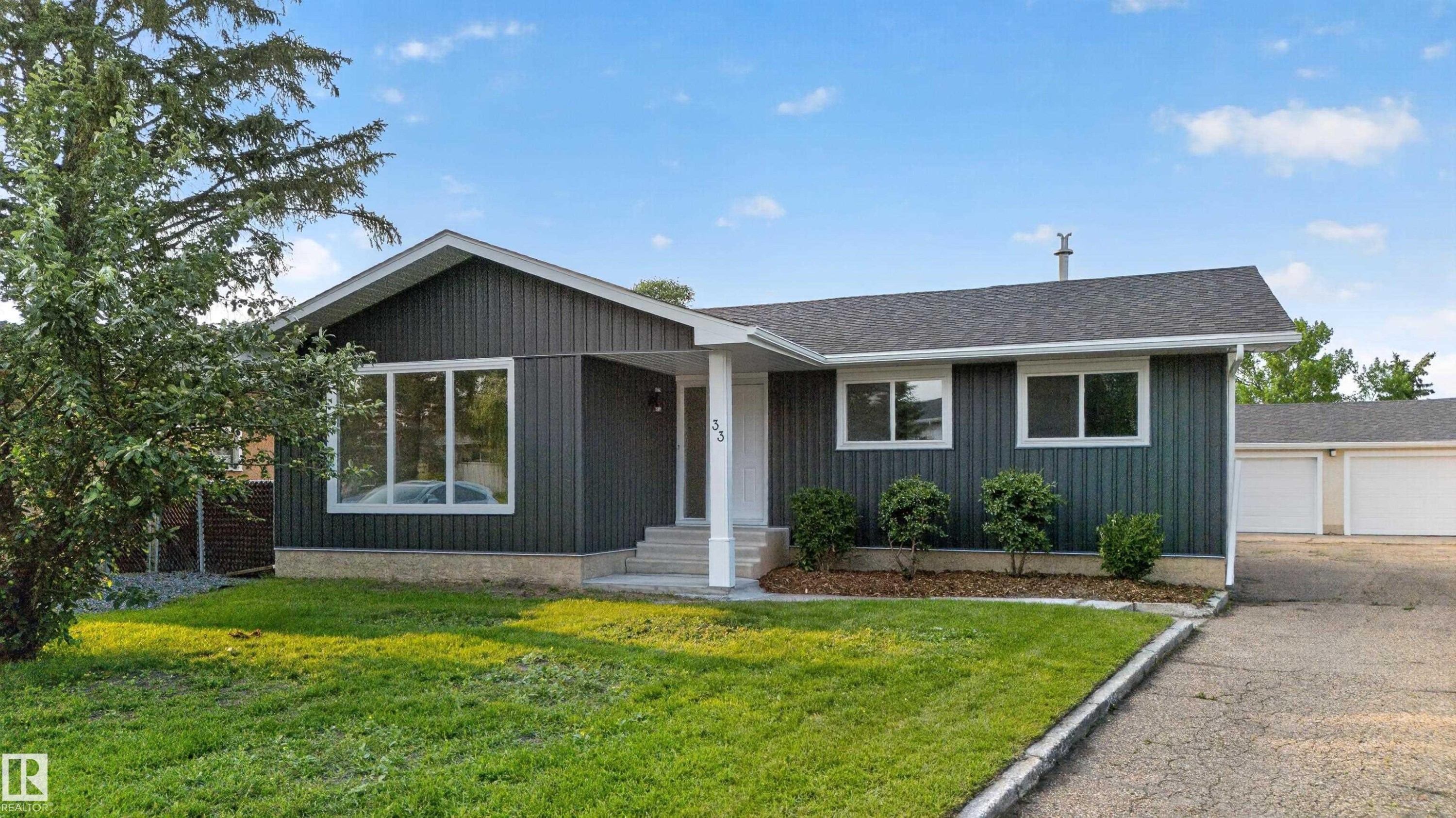 Contemporary bungalow featuring dark vertical siding, a multi-pane picture window, and a light gray shingle roof - 33 Brookside Avenue, Spruce Grove, AB
