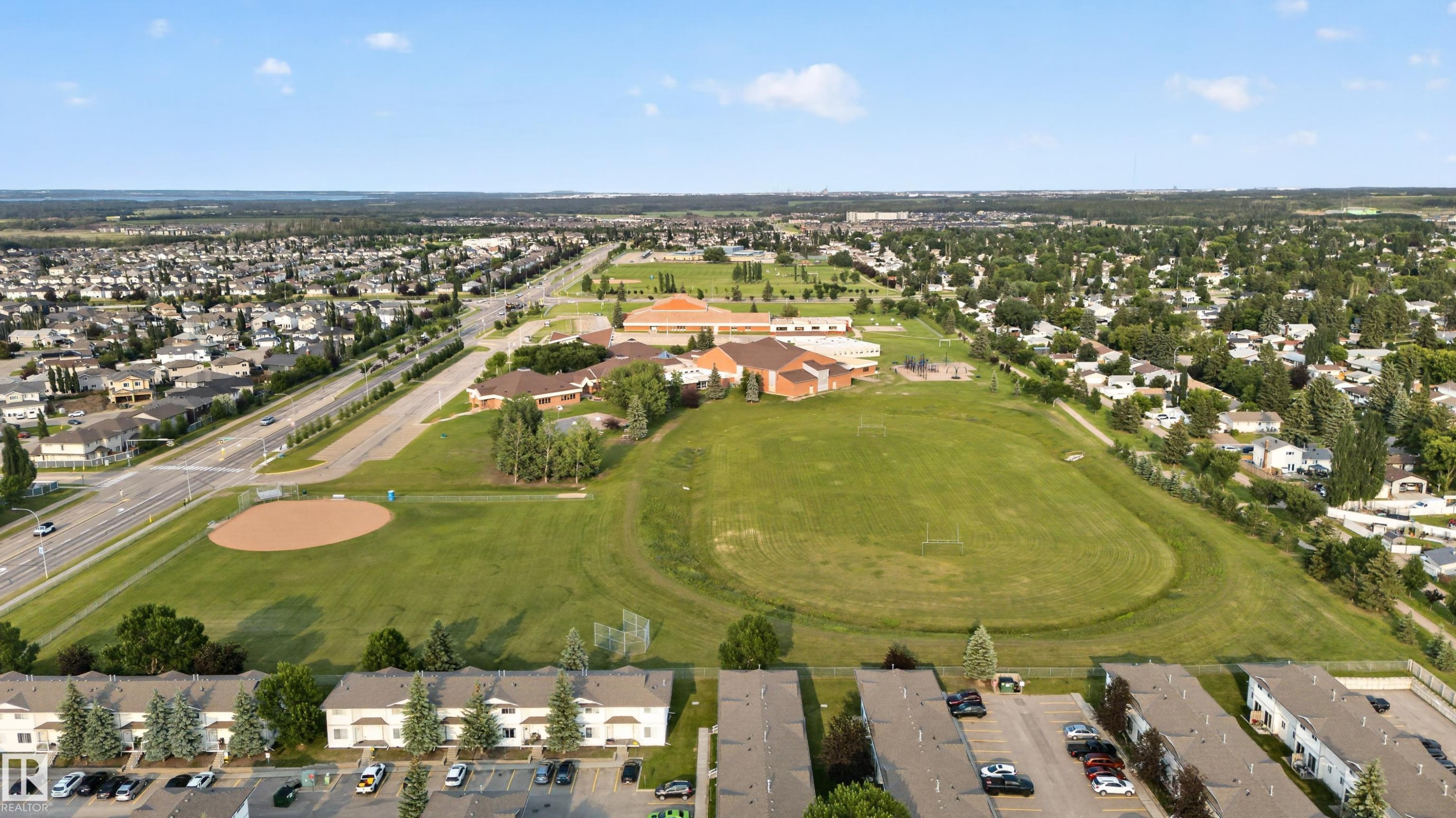 Expansive aerial panorama showcasing a residential community with abundant green spaces, including a large playing field and a baseball diamond - 33 Brookside Avenue, Spruce Grove, AB