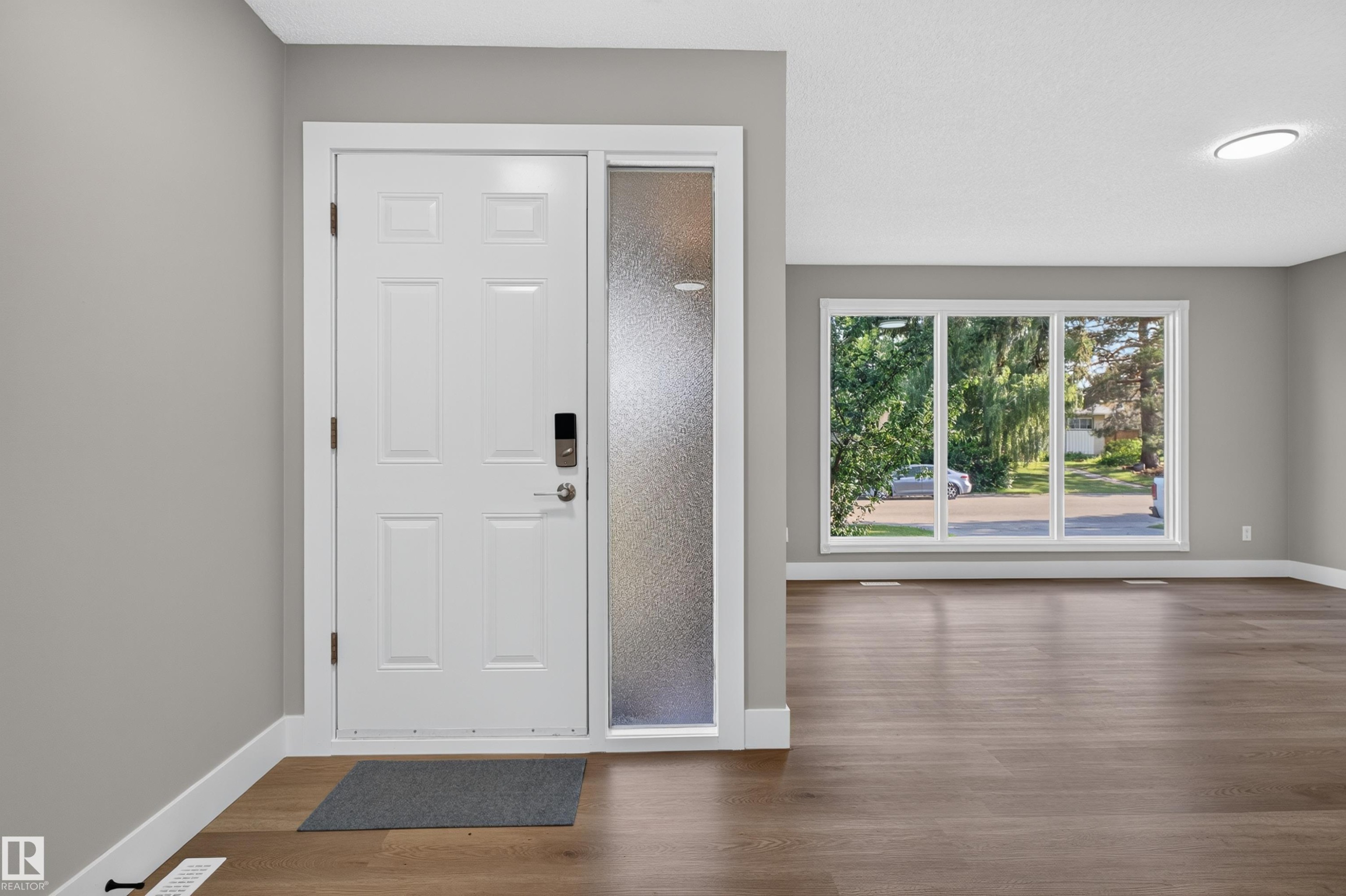 Entryway with a white paneled door featuring a digital lock, frosted sidelight, and wood-finish flooring - 33 Brookside Avenue, Spruce Grove, AB