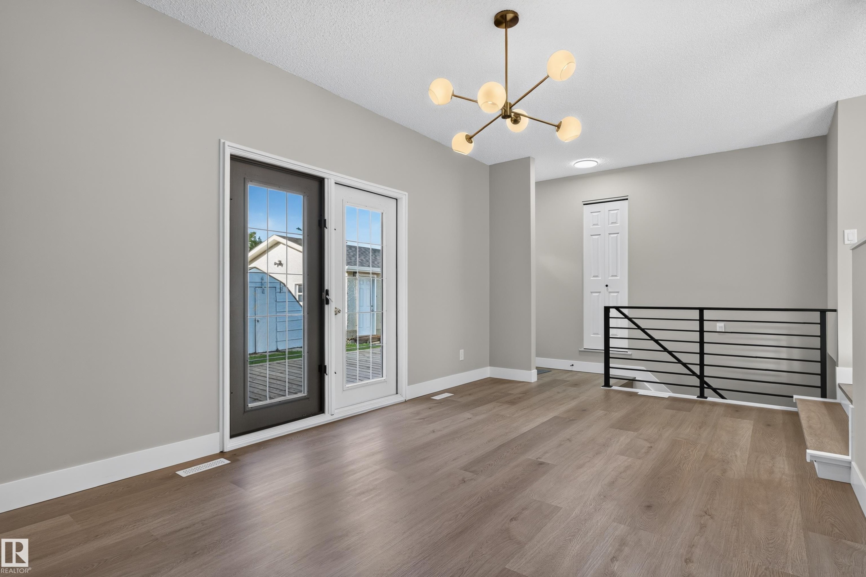 Spacious room featuring wood-finish flooring, light grey walls, and a contemporary brass chandelier - 33 Brookside Avenue, Spruce Grove, AB