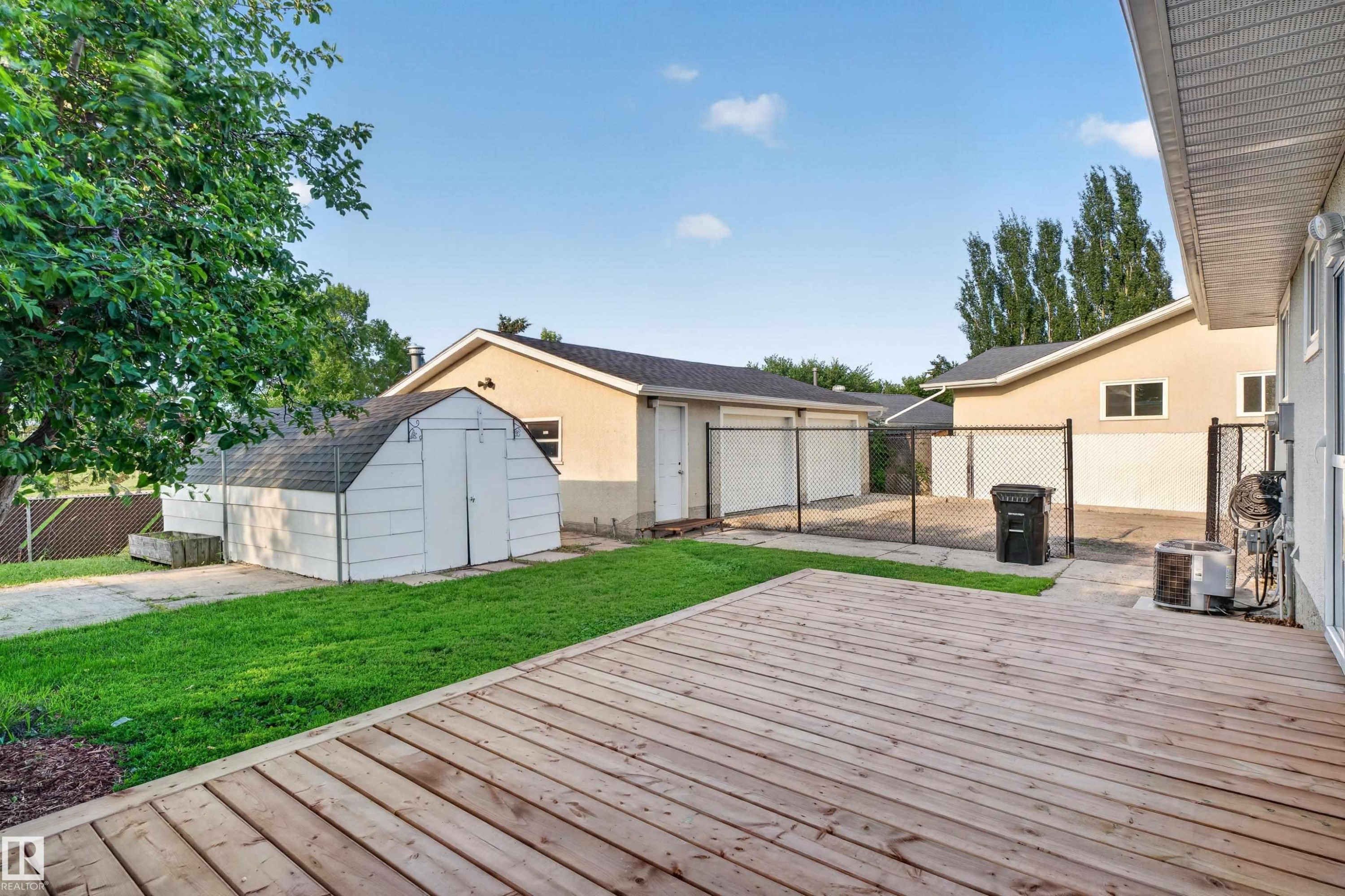 Expansive backyard featuring a natural wood deck, green lawn area, and a white storage shed - 33 Brookside Avenue, Spruce Grove, AB