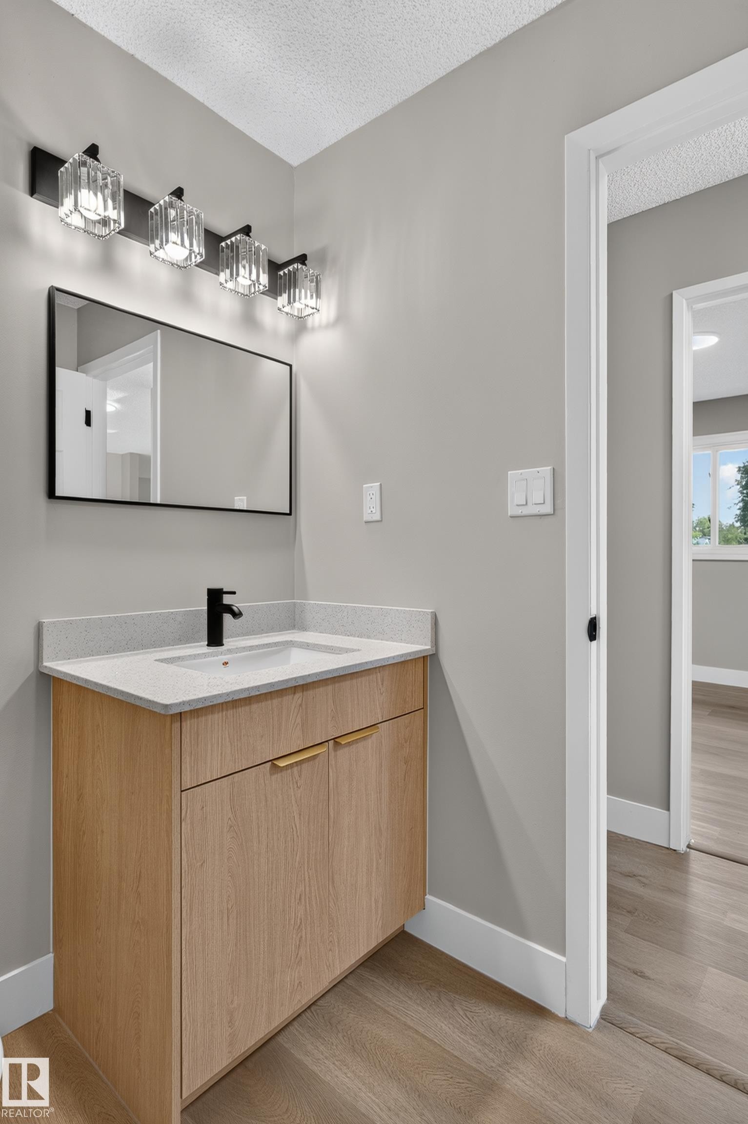 Bathroom vanity featuring a light wood-finish cabinet with gold-toned hardware, a light-toned countertop, and an integrated white sink - 33 Brookside Avenue, Spruce Grove, AB