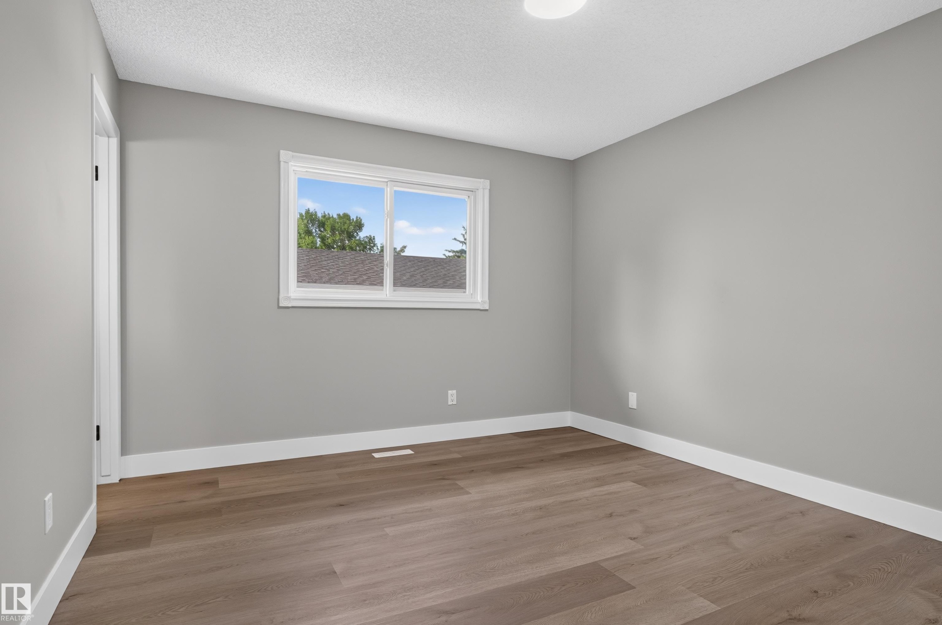 Room featuring wood-finish flooring, light grey painted walls, white baseboards, and a white window frame - 33 Brookside Avenue, Spruce Grove, AB