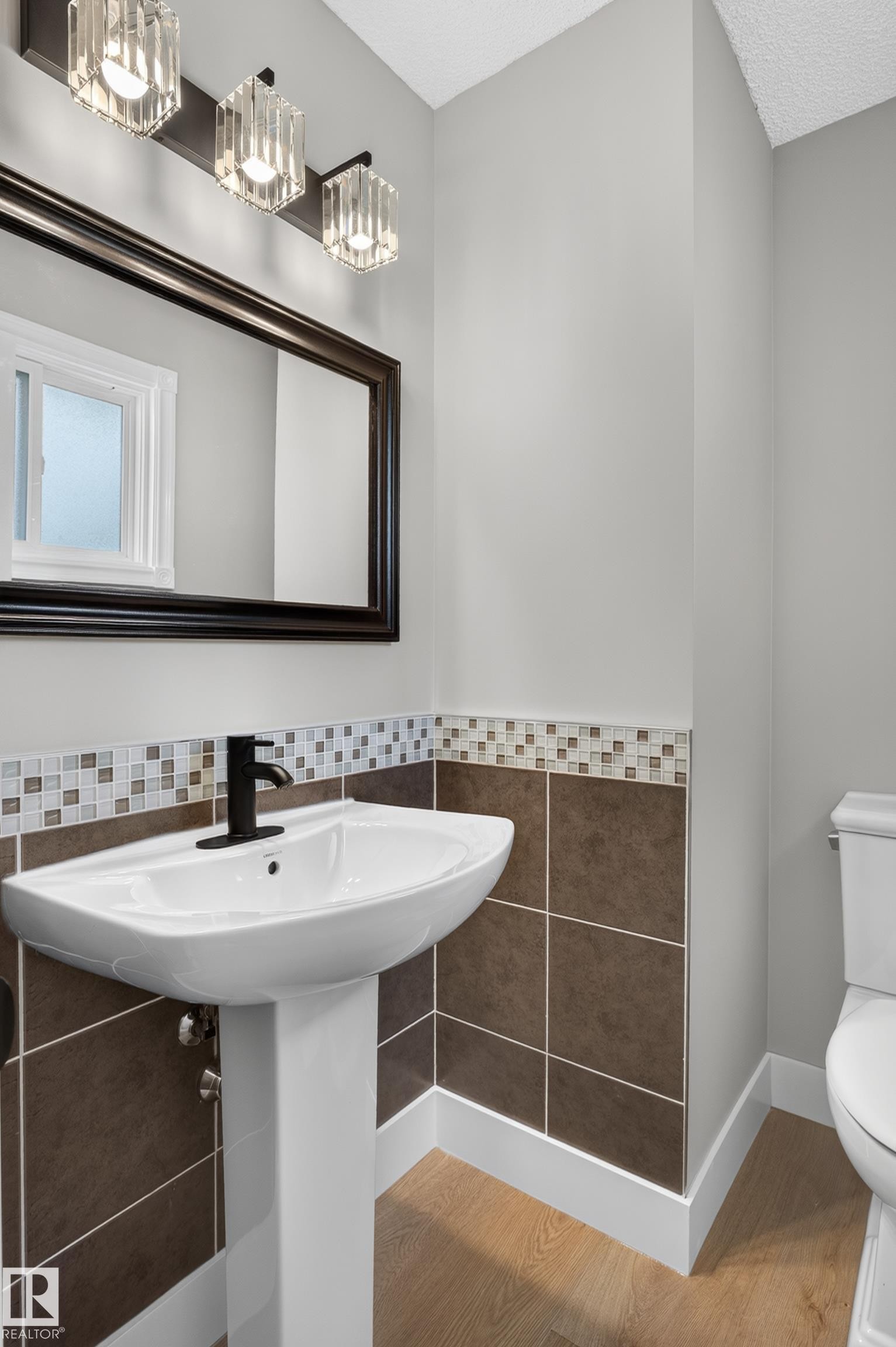 Pedestal sink with matte black faucet, set against a tiled wainscoting and mosaic border - 33 Brookside Avenue, Spruce Grove, AB