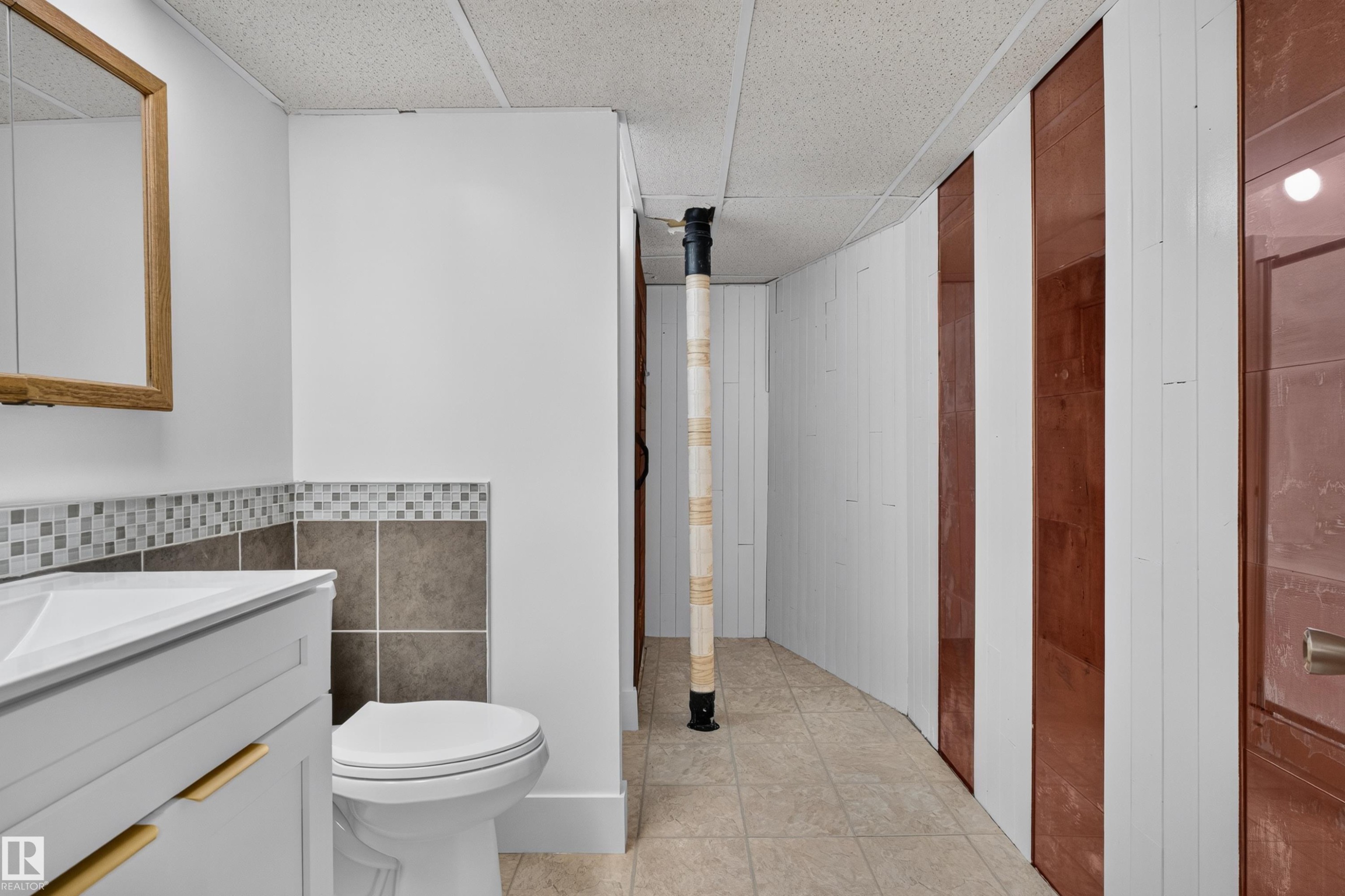 Bathroom vanity featuring a white rectangular sink, wood-framed mirror, and a mosaic tile backsplash - 33 Brookside Avenue, Spruce Grove, AB