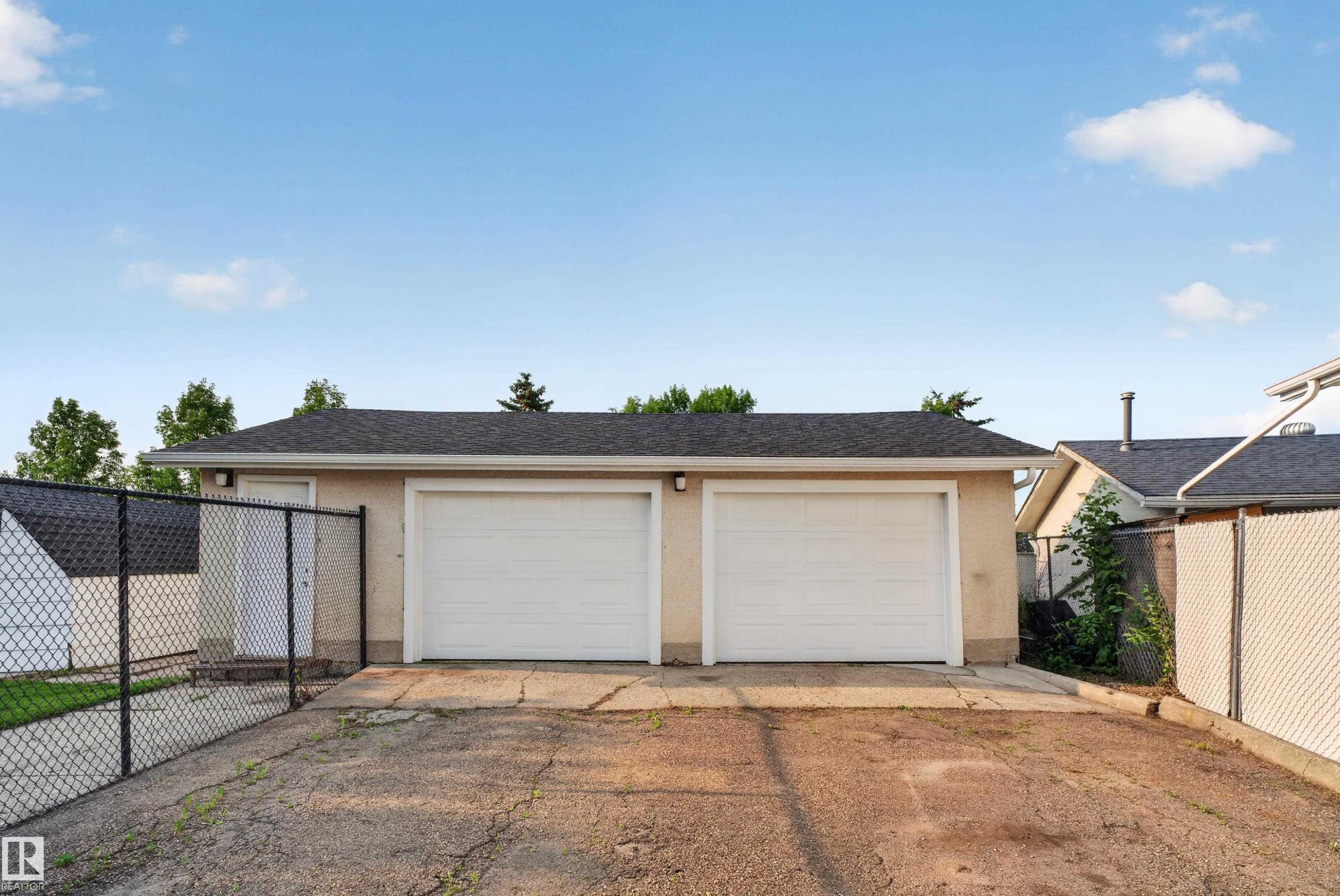Detached two-car garage with asphalt shingle roofing, beige stucco exterior, and chain-link fencing - 33 Brookside Avenue, Spruce Grove, AB