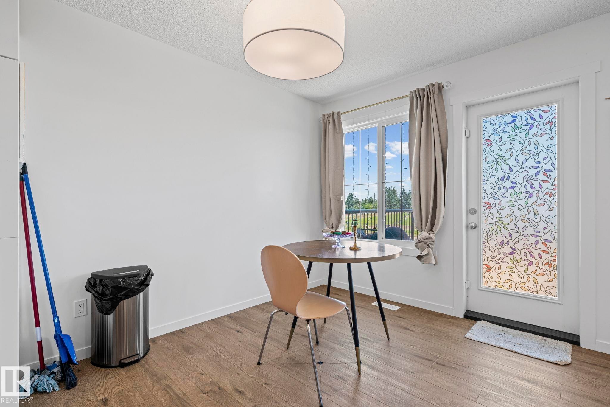 Bright dining area featuring wood-finish flooring, a contemporary drum ceiling light, and a window with outdoor views - 16 19904 31 Avenue, Edmonton, AB