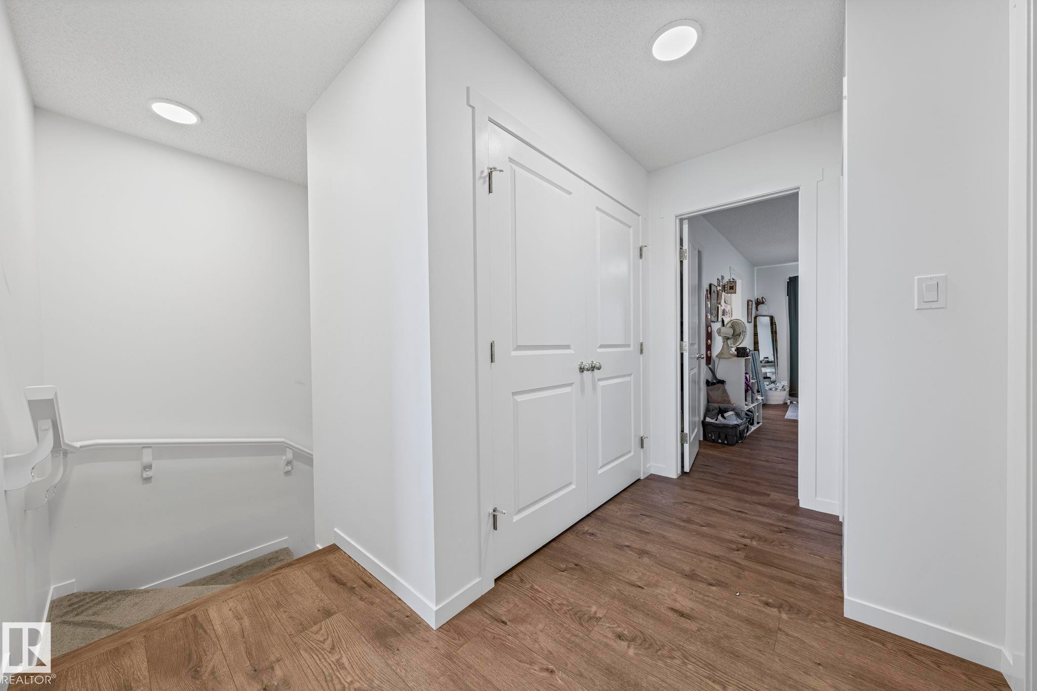 Hallway featuring wood-finish flooring, recessed lighting, white trim, and a white paneled door - 16 19904 31 Avenue, Edmonton, AB
