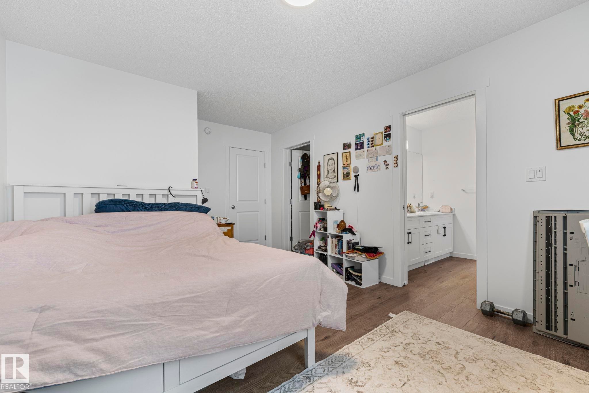 Bedroom featuring wood-finish flooring, white walls, and an attached bathroom with a single vanity and white cabinetry - 16 19904 31 Avenue, Edmonton, AB