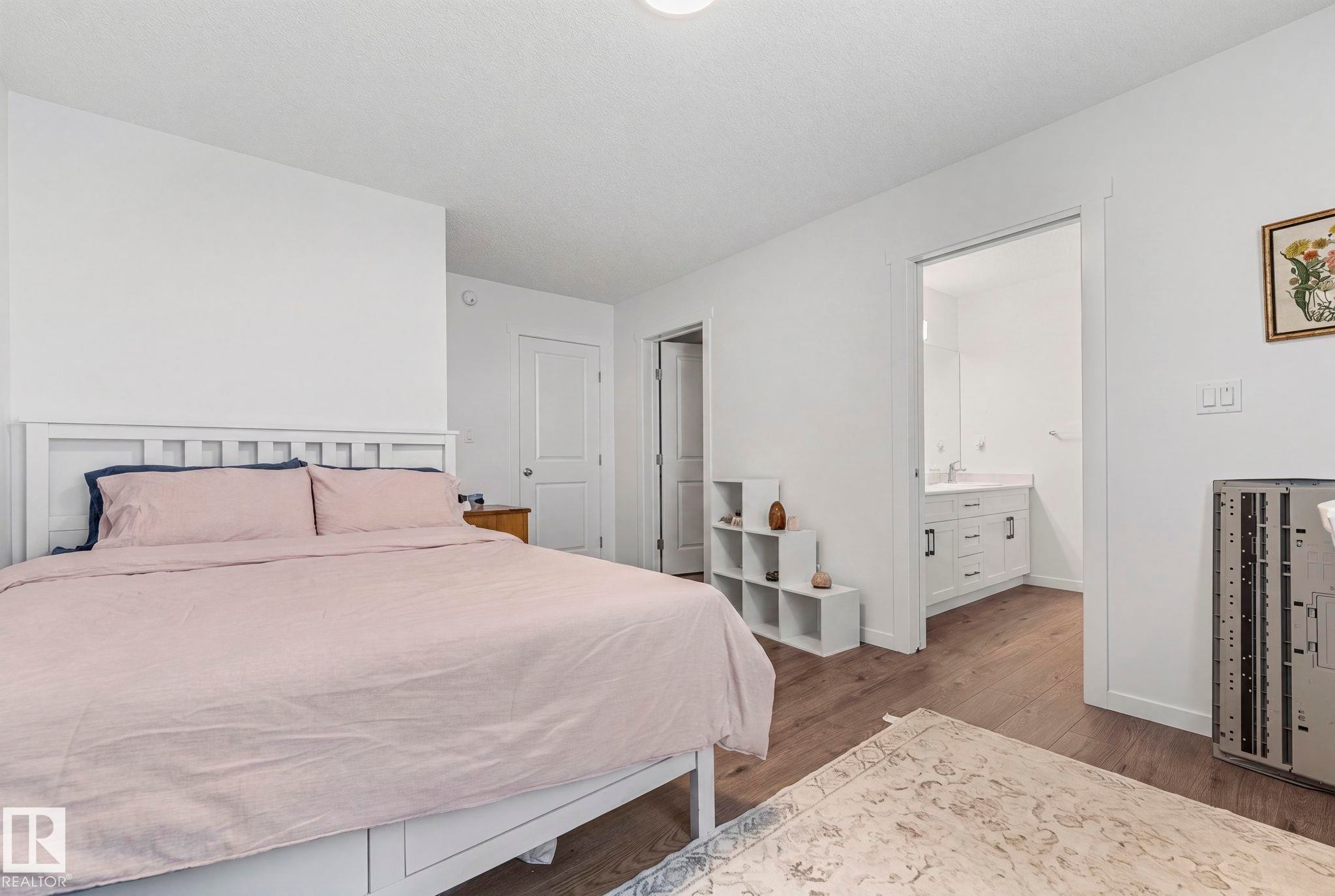 Spacious bedroom featuring wood-finish flooring and a white headboard - 16 19904 31 Avenue, Edmonton, AB