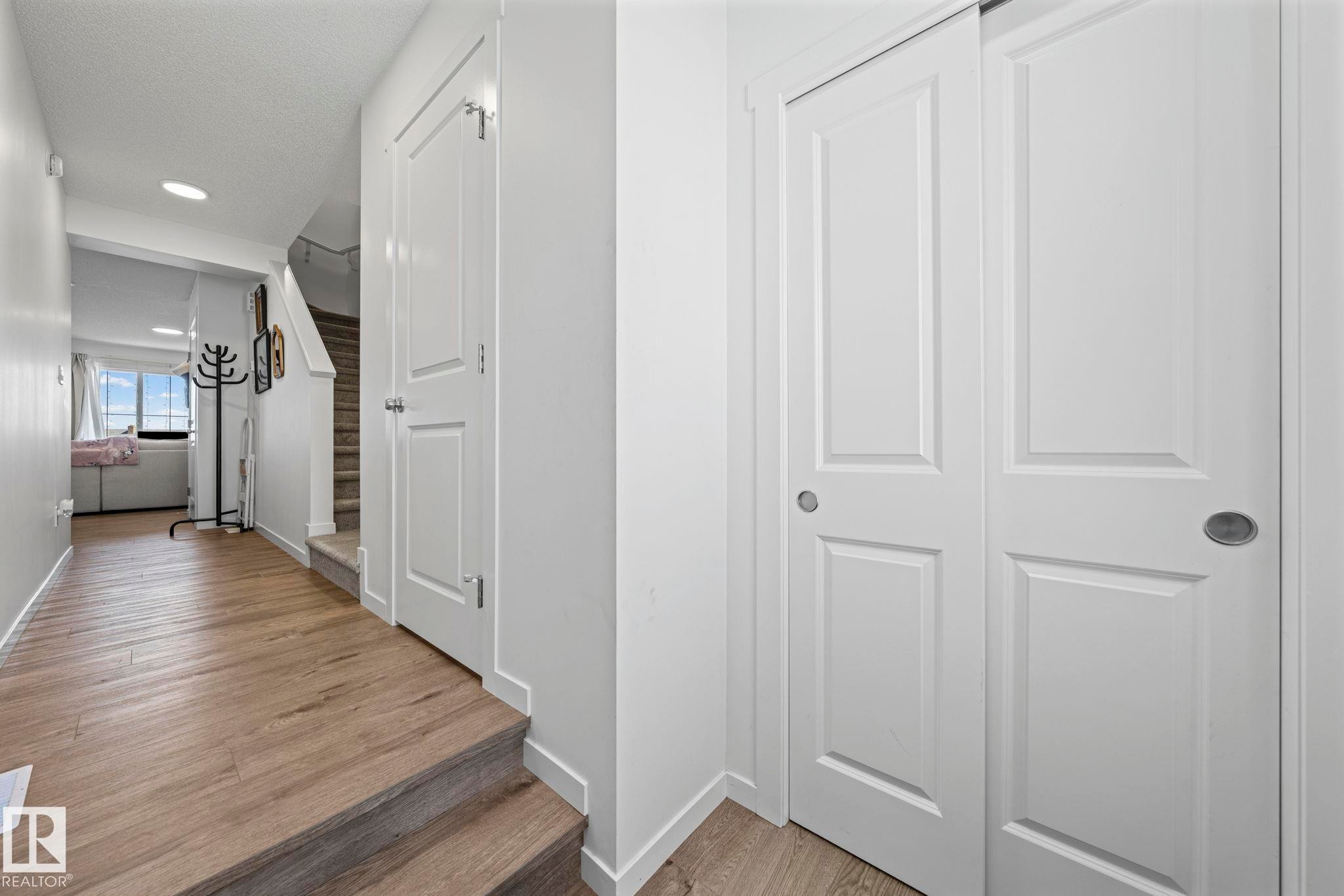 Hardwood-finish flooring extending from the hallway, featuring white paneled doors with brushed nickel hardware - 16 19904 31 Avenue, Edmonton, AB