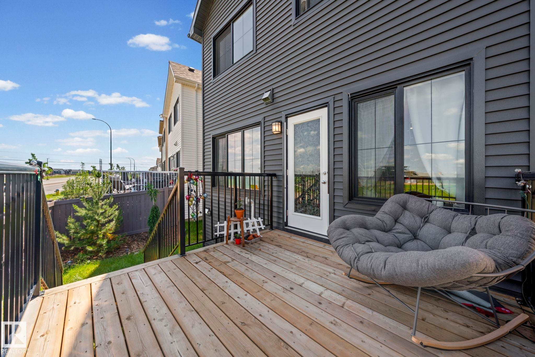 Wood-finish deck with black metal railing, featuring a white exterior door with glass insert, black siding, and multiple windows - 16 19904 31 Avenue, Edmonton, AB