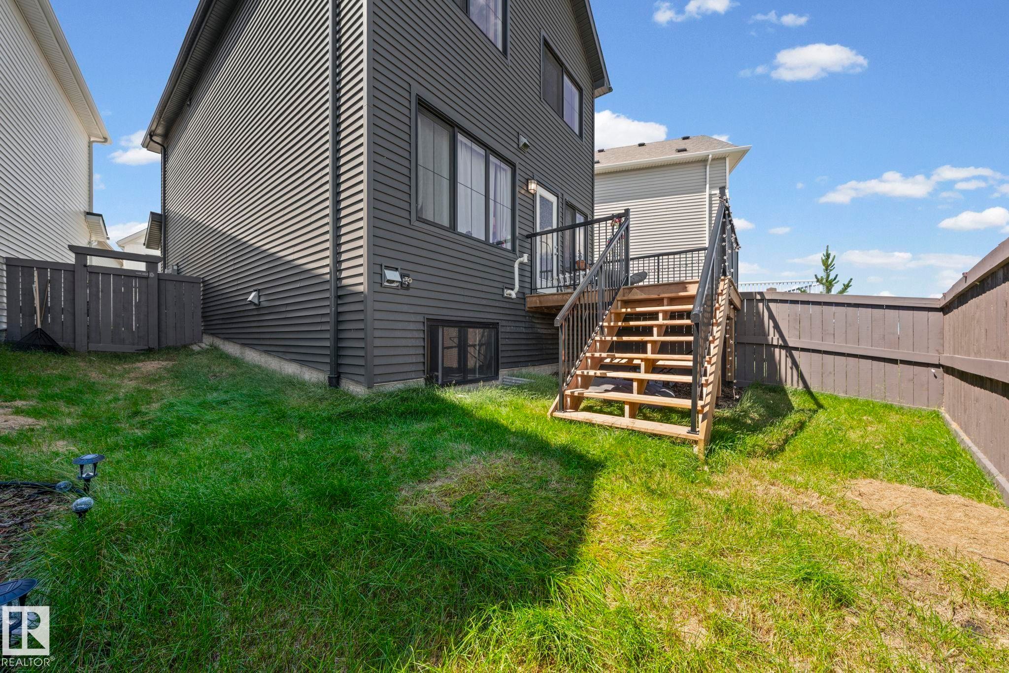 Exterior deck with wooden stairs, black metal railings, and a sliding glass door - 16 19904 31 Avenue, Edmonton, AB