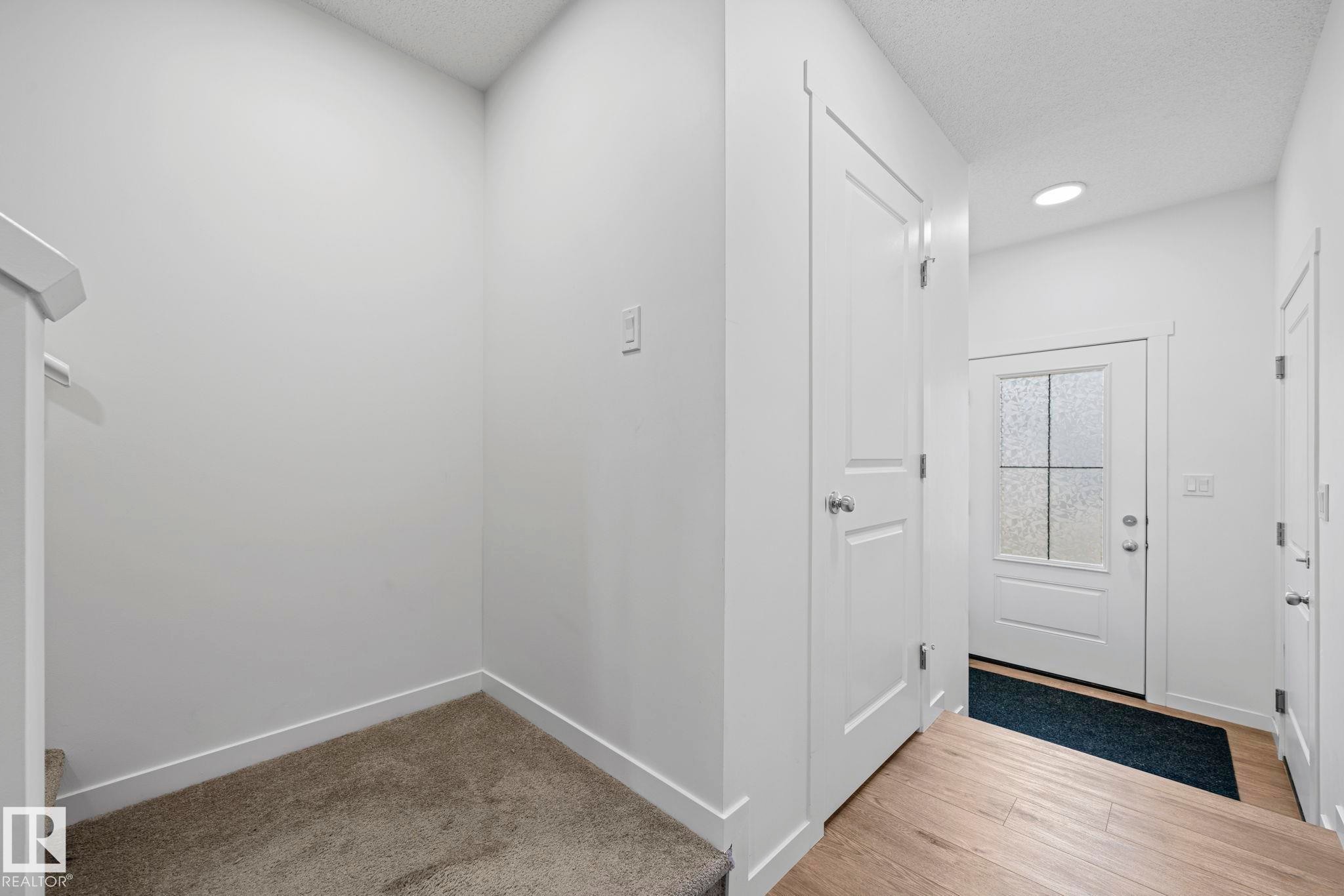 Entryway featuring a paneled door with frosted glass, recessed lighting, wood-finish flooring, and a staircase with carpeted treads - 16 19904 31 Avenue, Edmonton, AB