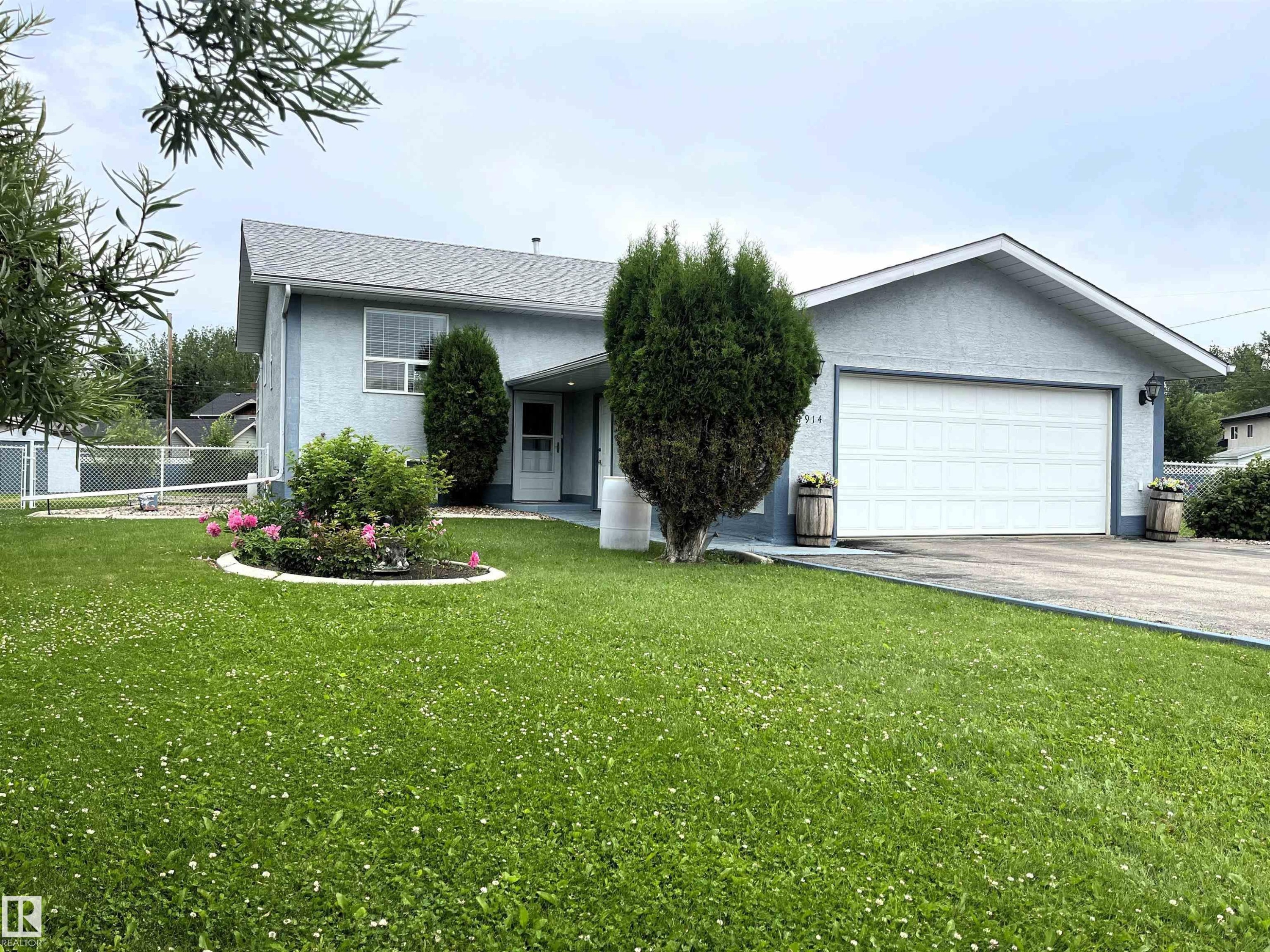 Light blue stucco exterior with a prominent attached two-car garage - 4914 51 Ave, Entwistle, AB