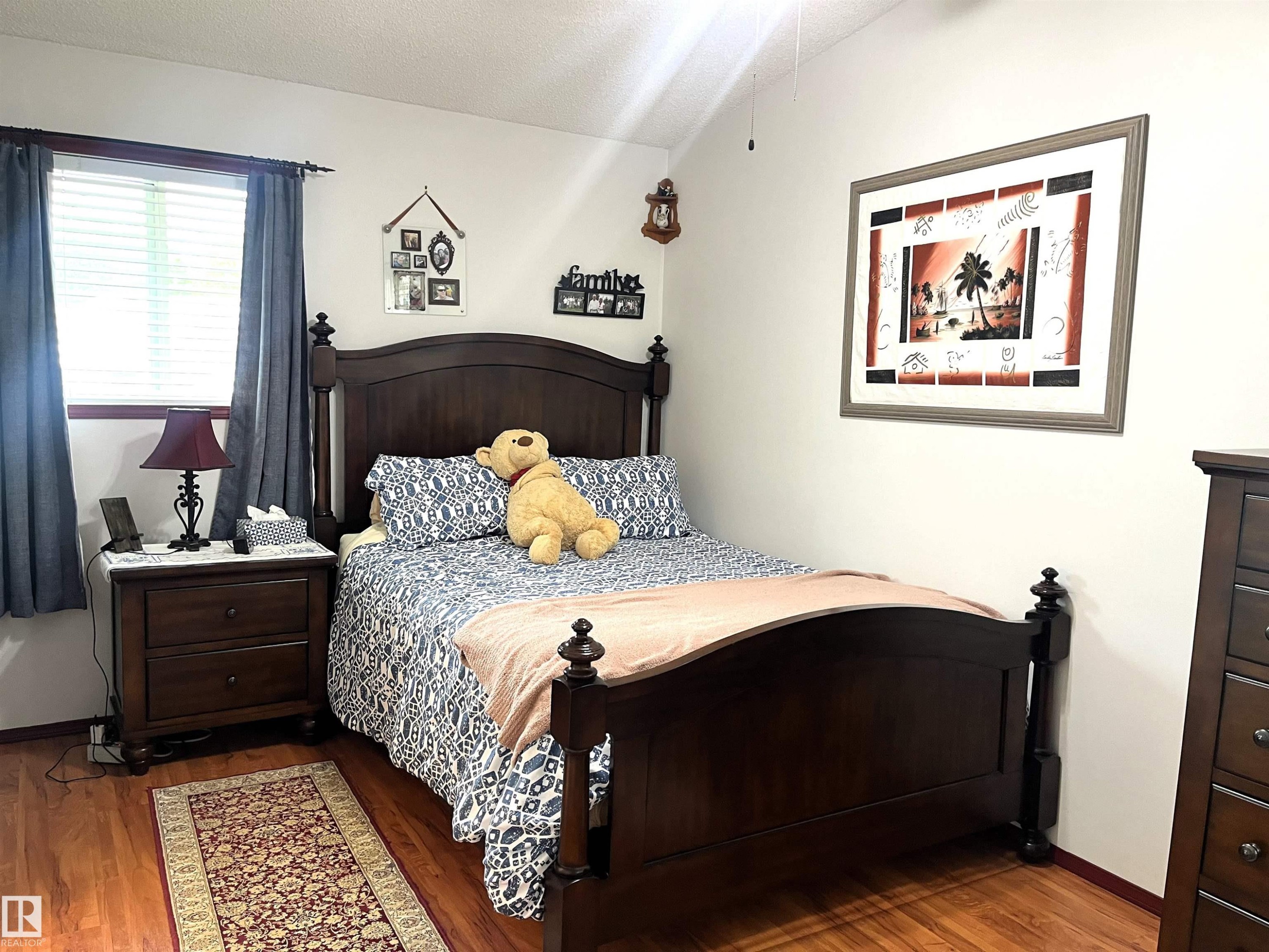 Bedroom featuring wood-finish flooring, a window with horizontal blinds, and a ceiling fan - 4914 51 Ave, Entwistle, AB