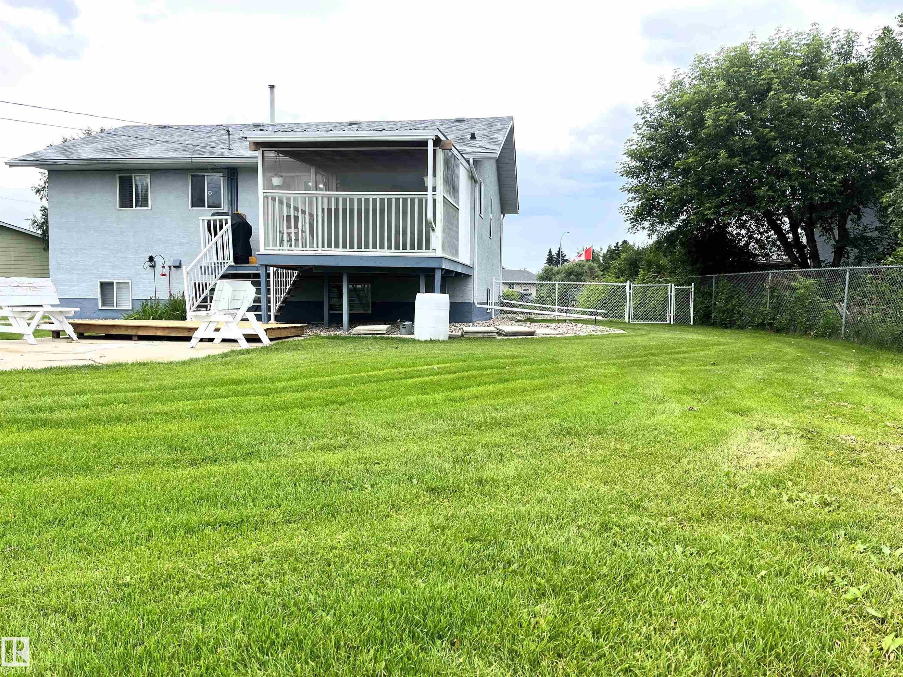 Spacious backyard featuring a manicured lawn, screened-in elevated deck, and lower wood deck - 4914 51 Ave, Entwistle, AB