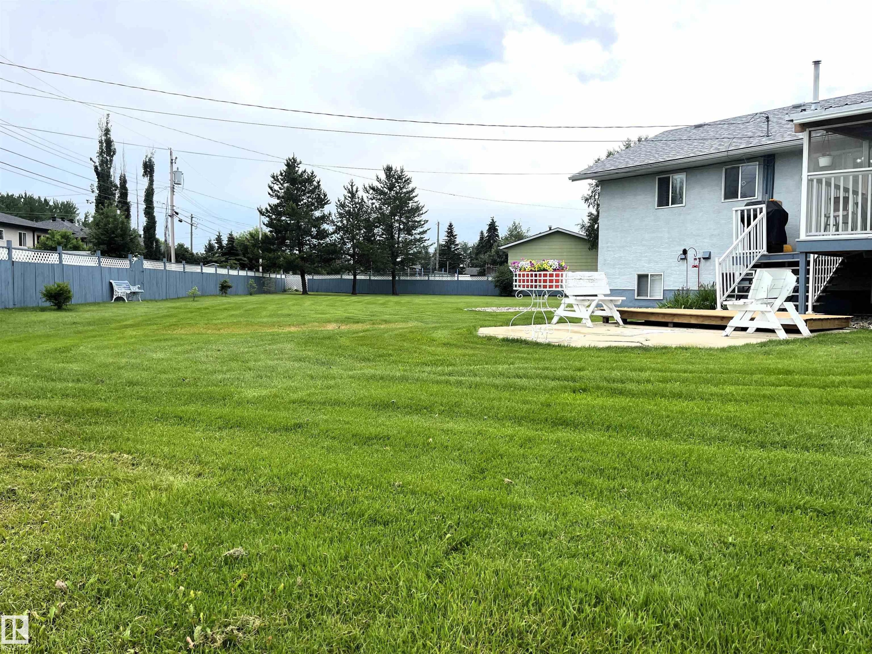 Expansive green lawn with a blue perimeter fence - 4914 51 Ave, Entwistle, AB