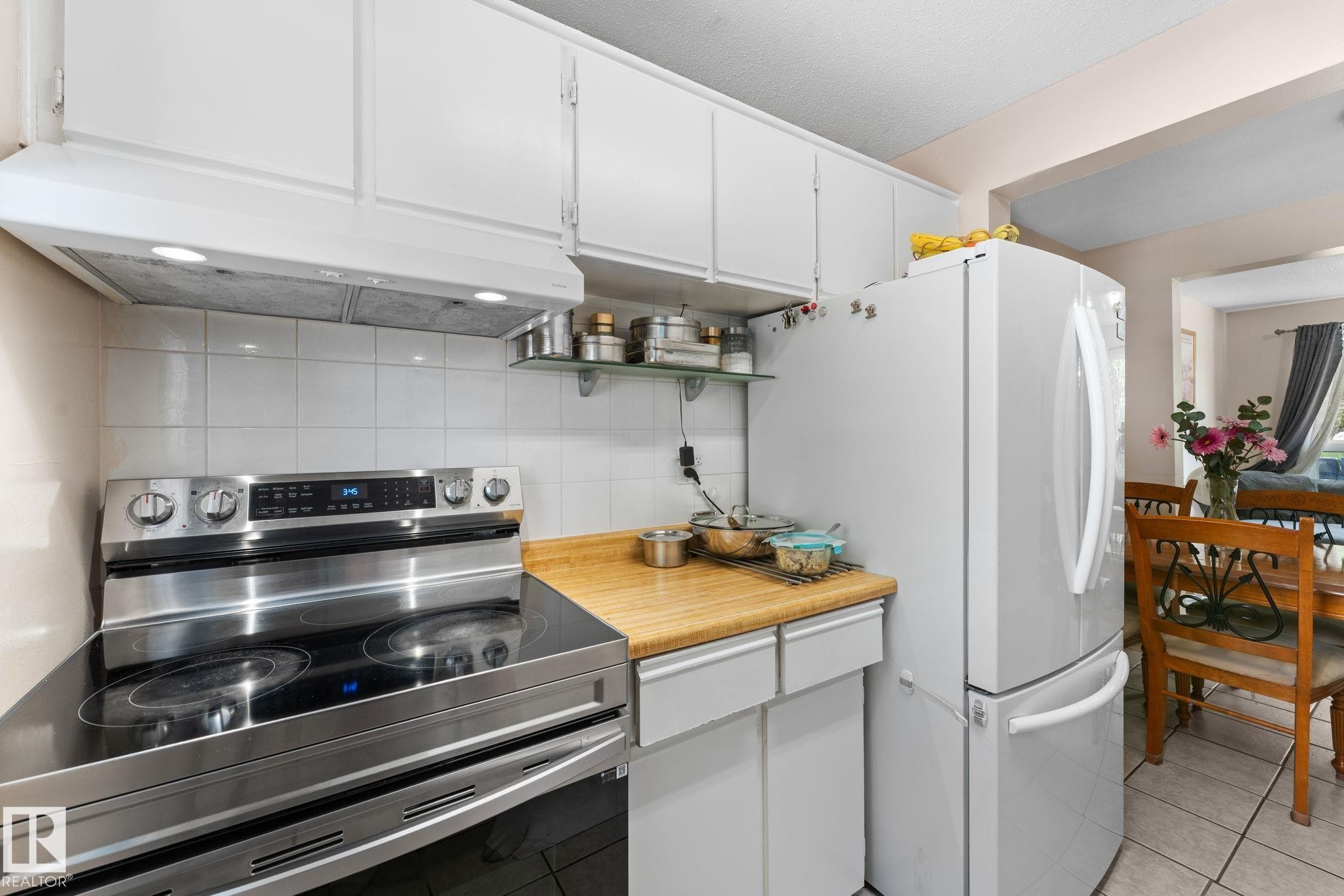 Kitchen featuring white cabinetry, a stainless steel range with a flat cooktop, white tile backsplash, wood-finish countertops, and a white refrigerator - 359 Northgate Terrace, Edmonton, AB
