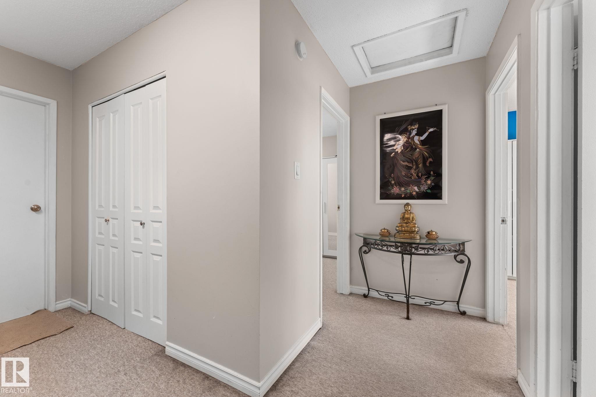 Hallway featuring neutral wall paint, light-toned carpet flooring, white bi-fold closet doors, white trim, and multiple doorways - 359 Northgate Terrace, Edmonton, AB