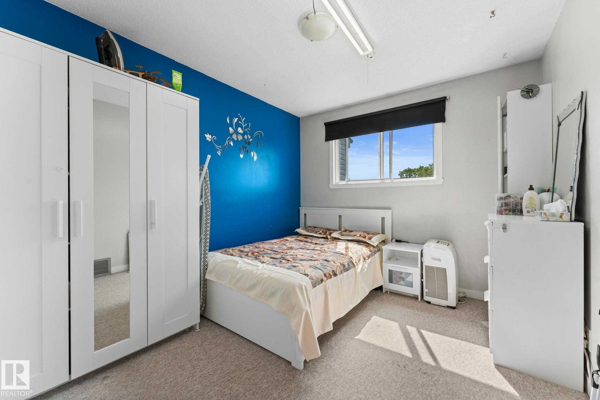 Carpeted bedroom featuring a window with a roller shade, light-colored walls, and a blue accent wall - 359 Northgate Terrace, Edmonton, AB