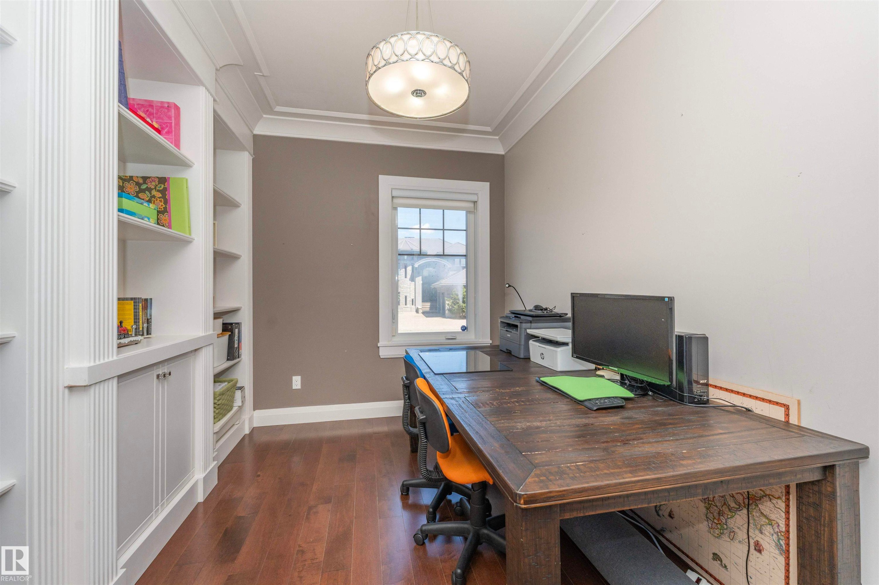 Room featuring extensive built-in shelving and cabinetry, wood-finish flooring, a window, crown molding, and a decorative ceiling light fixture - 3503 Watson Point(E), Edmonton, AB