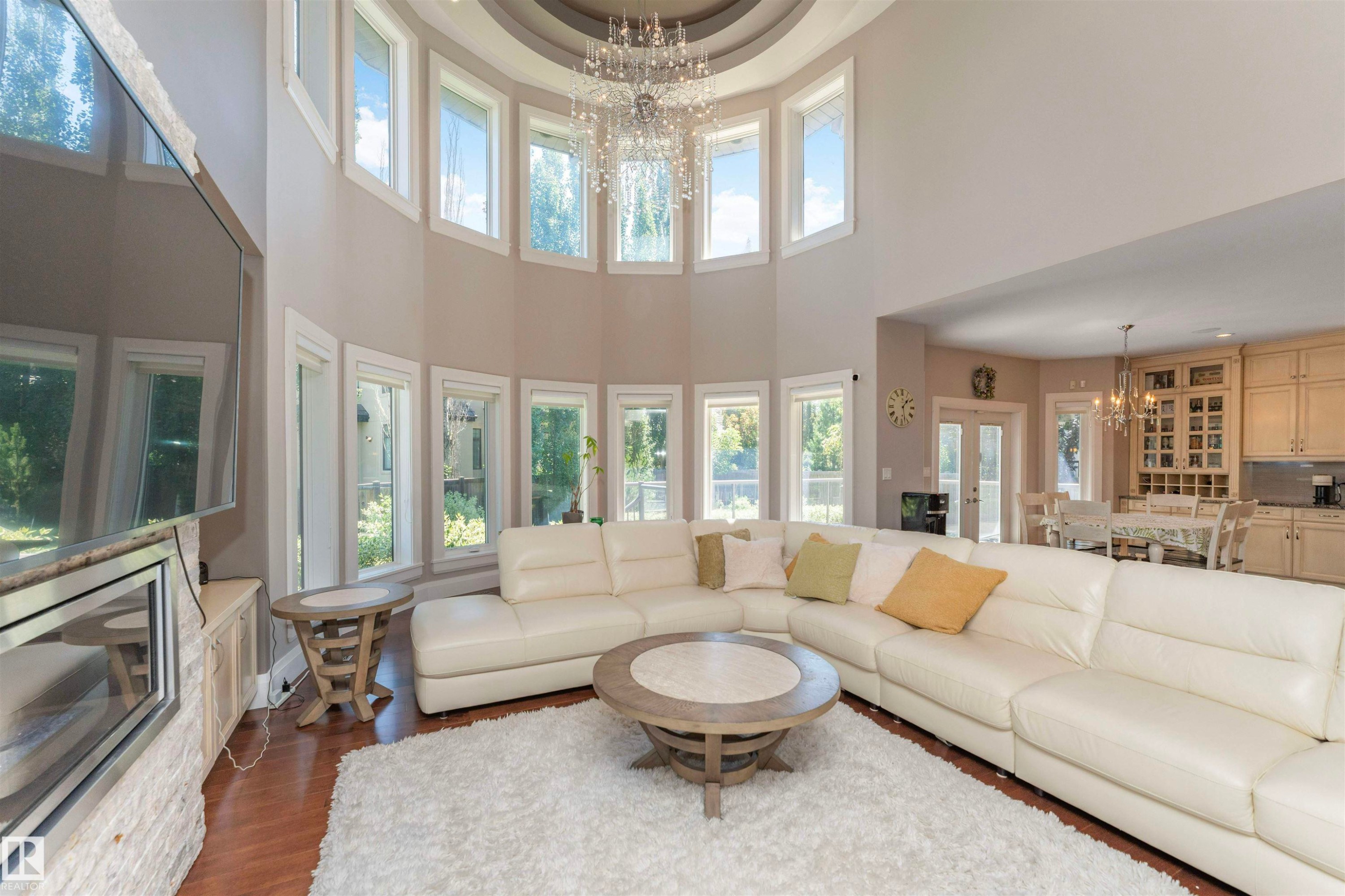 Two-story living area featuring a prominent chandelier, curved window wall, and wood-finish flooring - 3503 Watson Point(E), Edmonton, AB