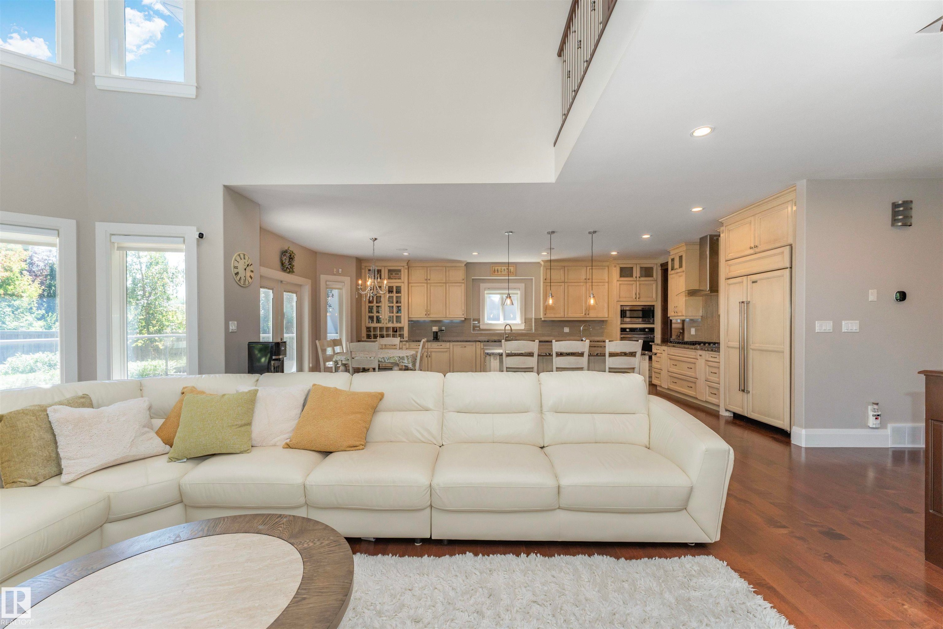 Open-concept living space featuring high ceilings, hardwood flooring, and a contemporary kitchen with light wood cabinetry and stainless steel appliances - 3503 Watson Point(E), Edmonton, AB
