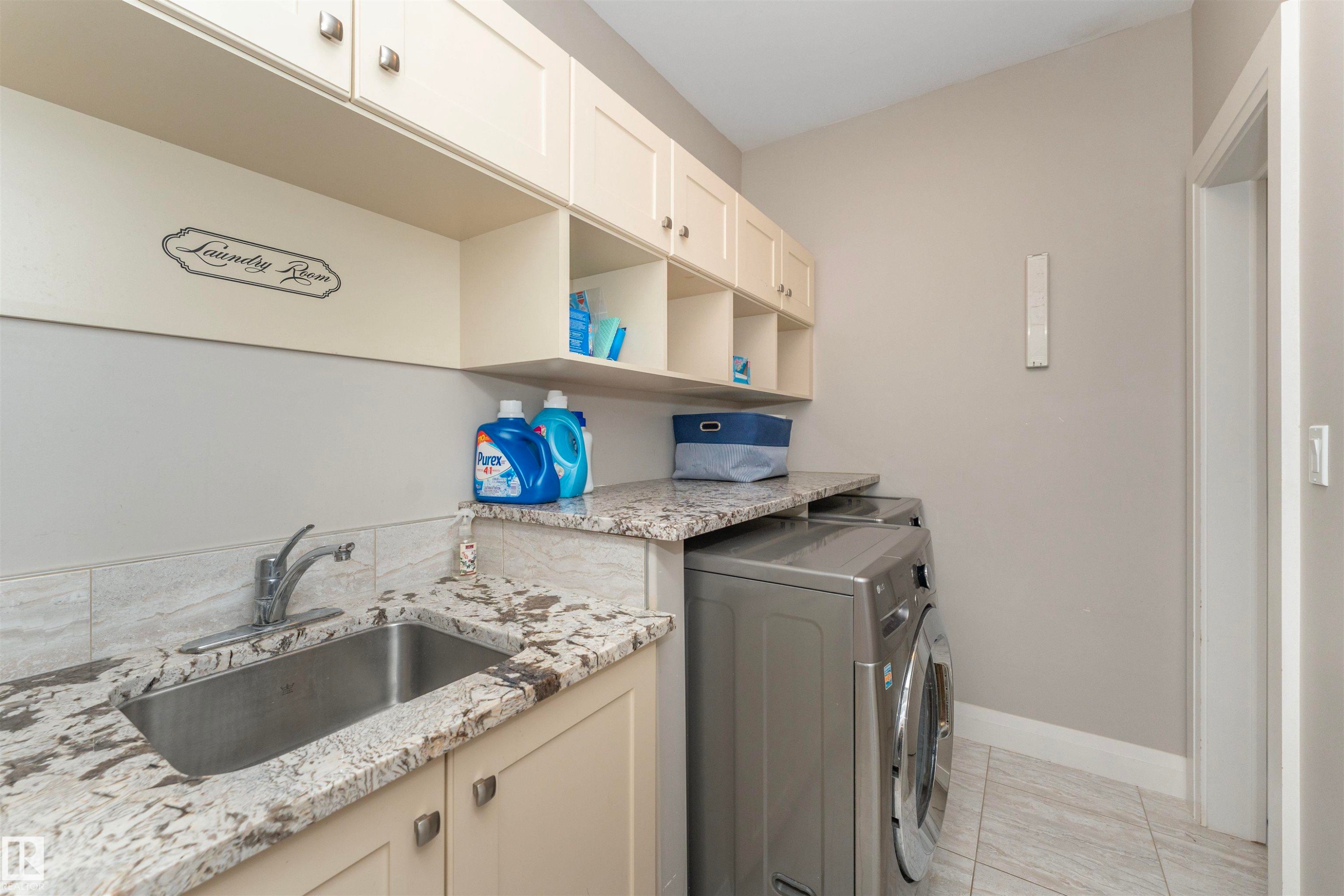 Dedicated laundry space featuring a built-in stainless steel sink, granite-finish countertop, and extensive upper cabinetry with integrated open shelving - 3503 Watson Point(E), Edmonton, AB