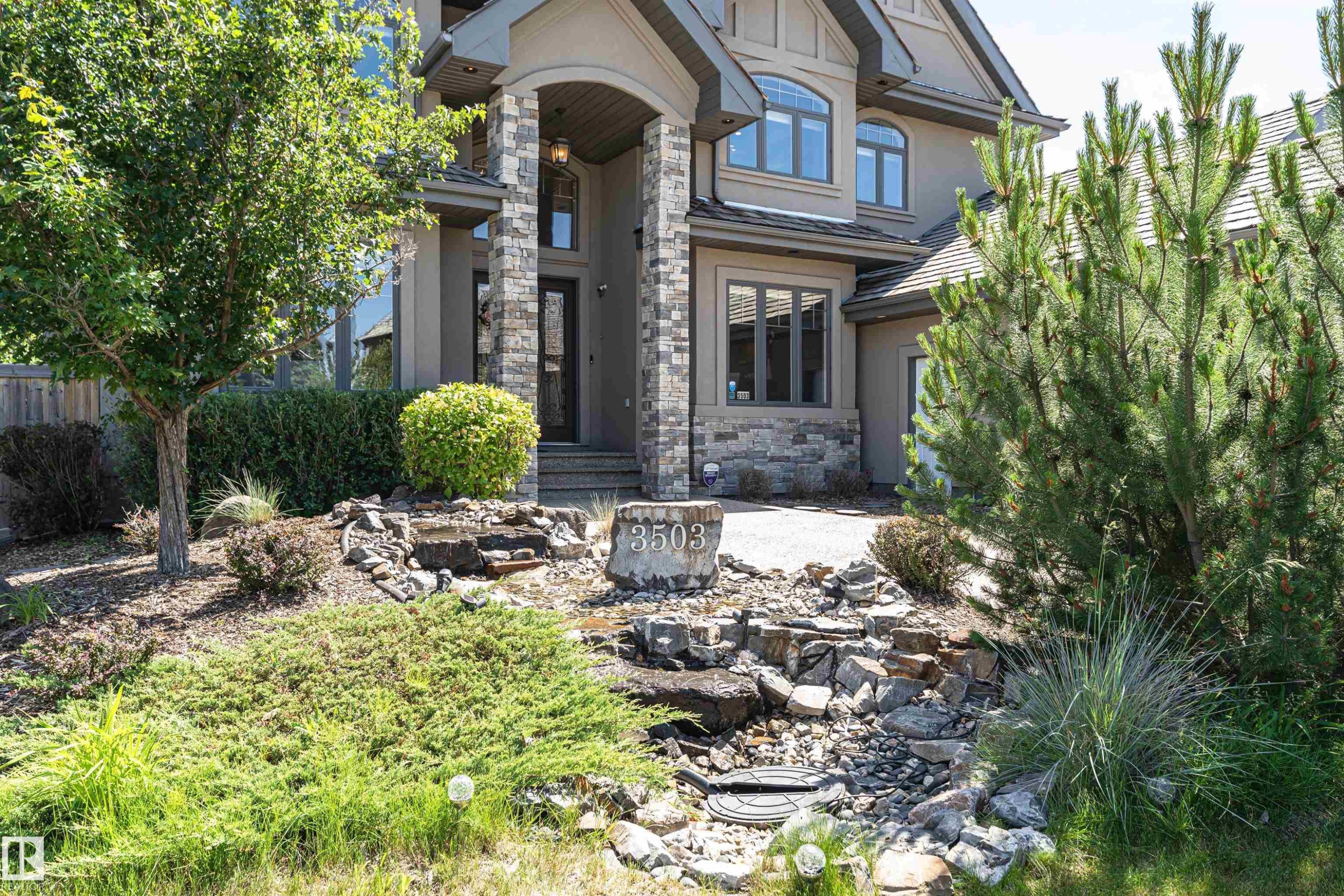 Stucco and stone exterior featuring an arched portico entryway, multiple window styles, and a gabled roofline - 3503 Watson Point(E), Edmonton, AB