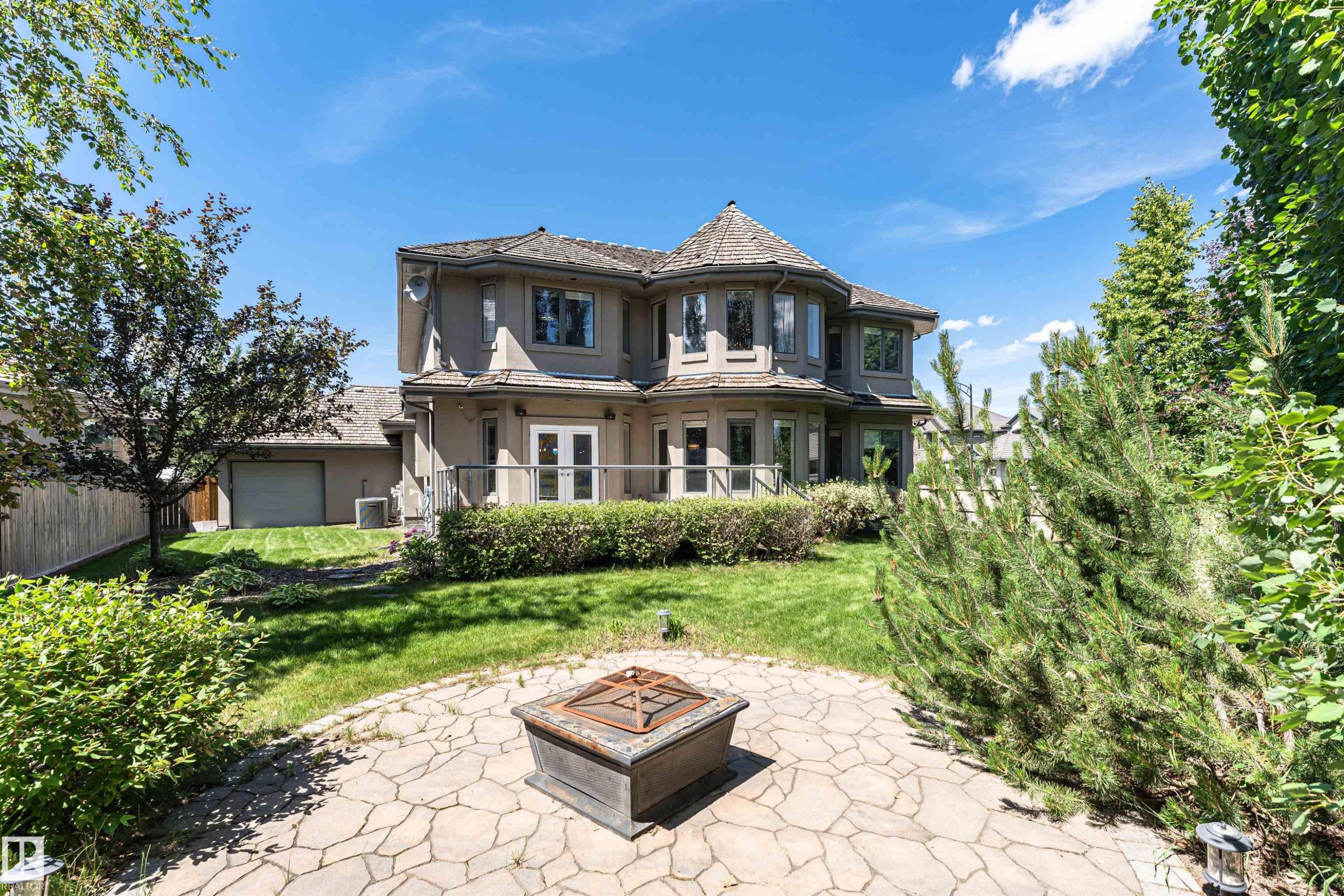 Exterior stucco residence featuring a multi-level deck, ground-level stone patio, and a domed turret with multiple windows - 3503 Watson Point(E), Edmonton, AB