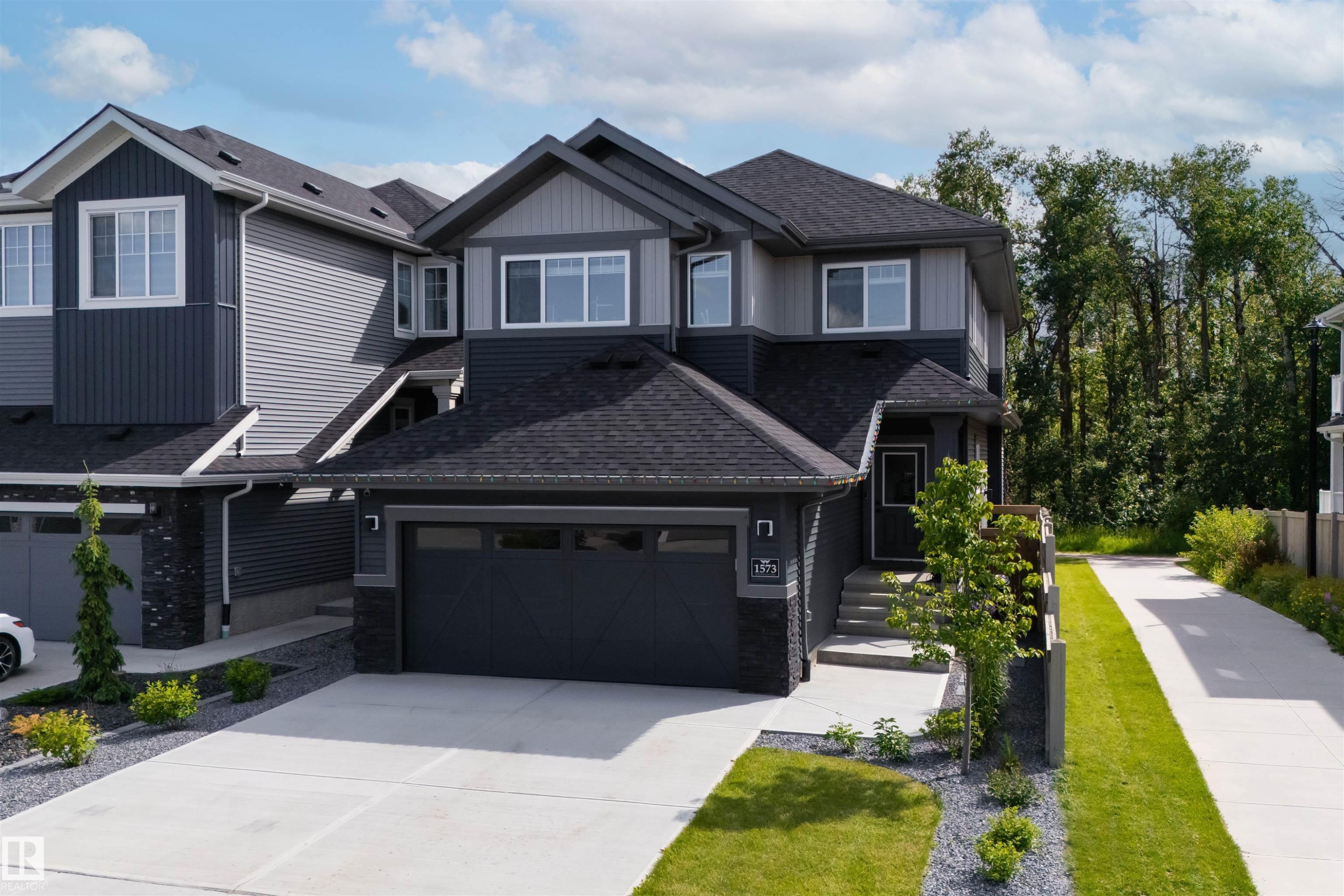 Contemporary two-story residence featuring a two-tone facade, attached garage with frosted glass panels, concrete driveway, and tiered landscaping with decorative stone - 1573 Esaiw Place Nw, Edmonton, AB