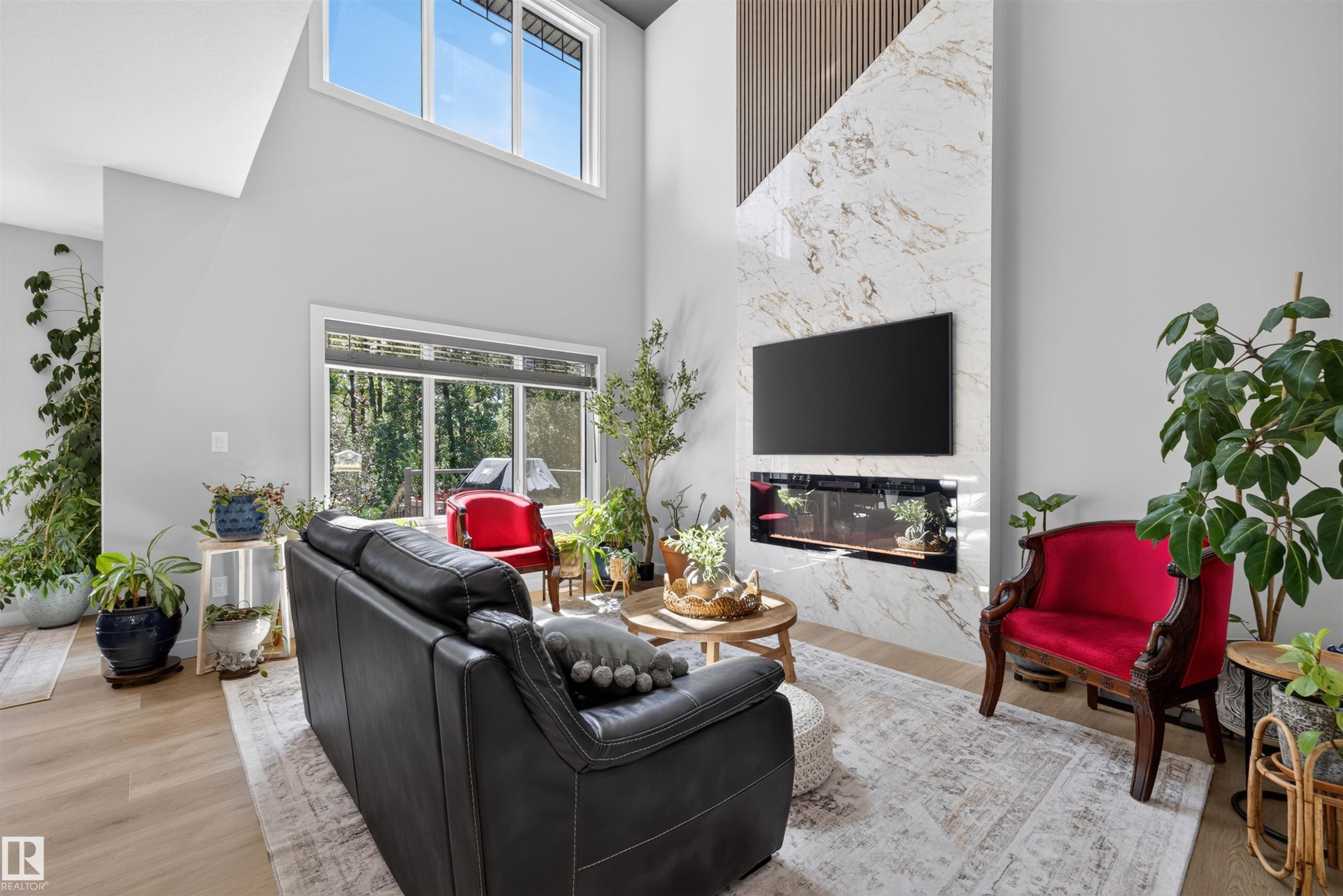 Vaulted ceilings featuring upper-level windows, large format tile fireplace surround with integrated linear firebox, light wood-finish flooring, and expansive rear windows - 1573 Esaiw Place Nw, Edmonton, AB