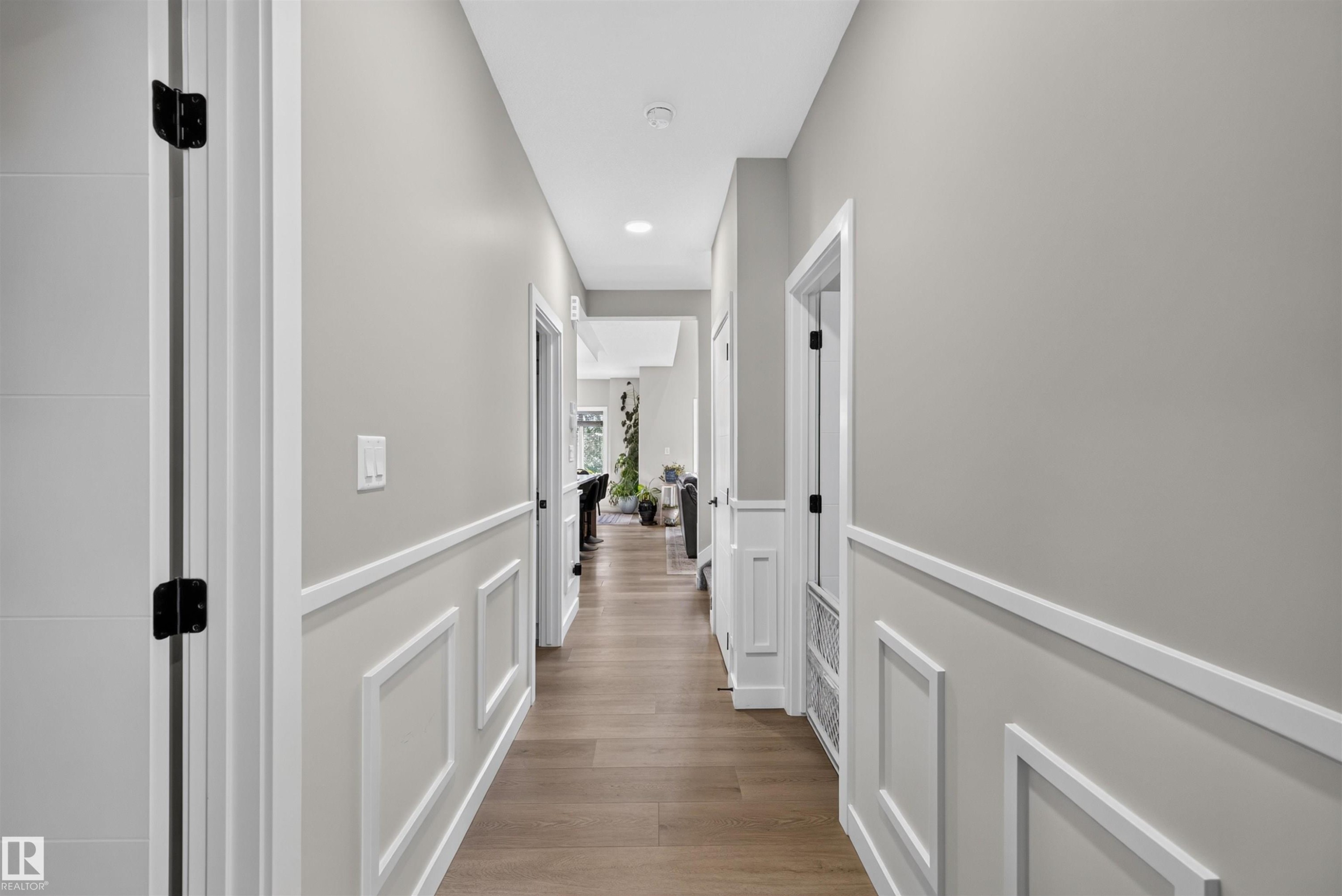Main Floor Hallway featuring panel molding, light gray walls, wood-finish flooring, white trim, and black door hardware - 1573 Esaiw Place Nw, Edmonton, AB