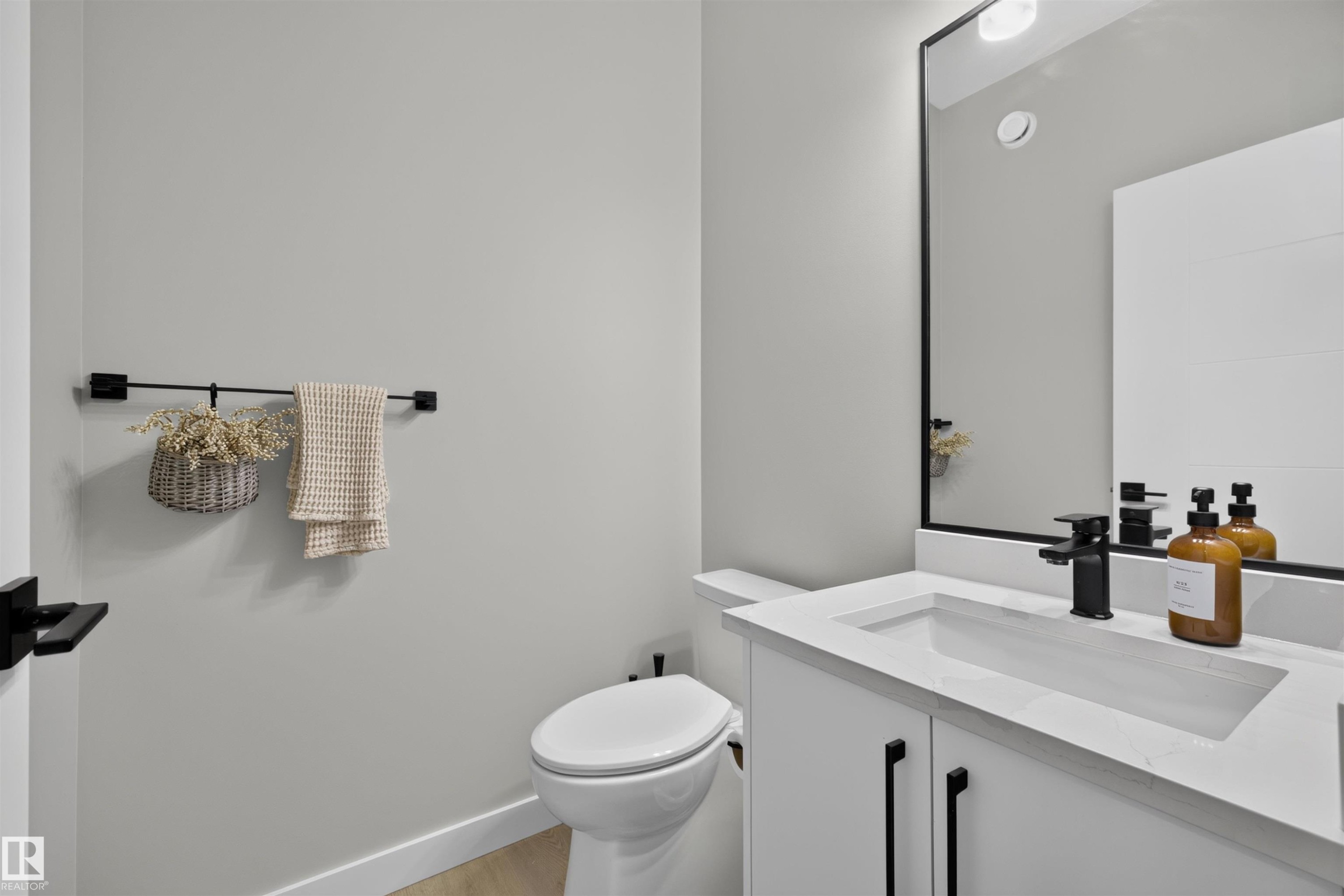 Modern powder room featuring a white vanity with integrated rectangular sink, matte black faucet, and coordinating black framed mirror - 1573 Esaiw Place Nw, Edmonton, AB