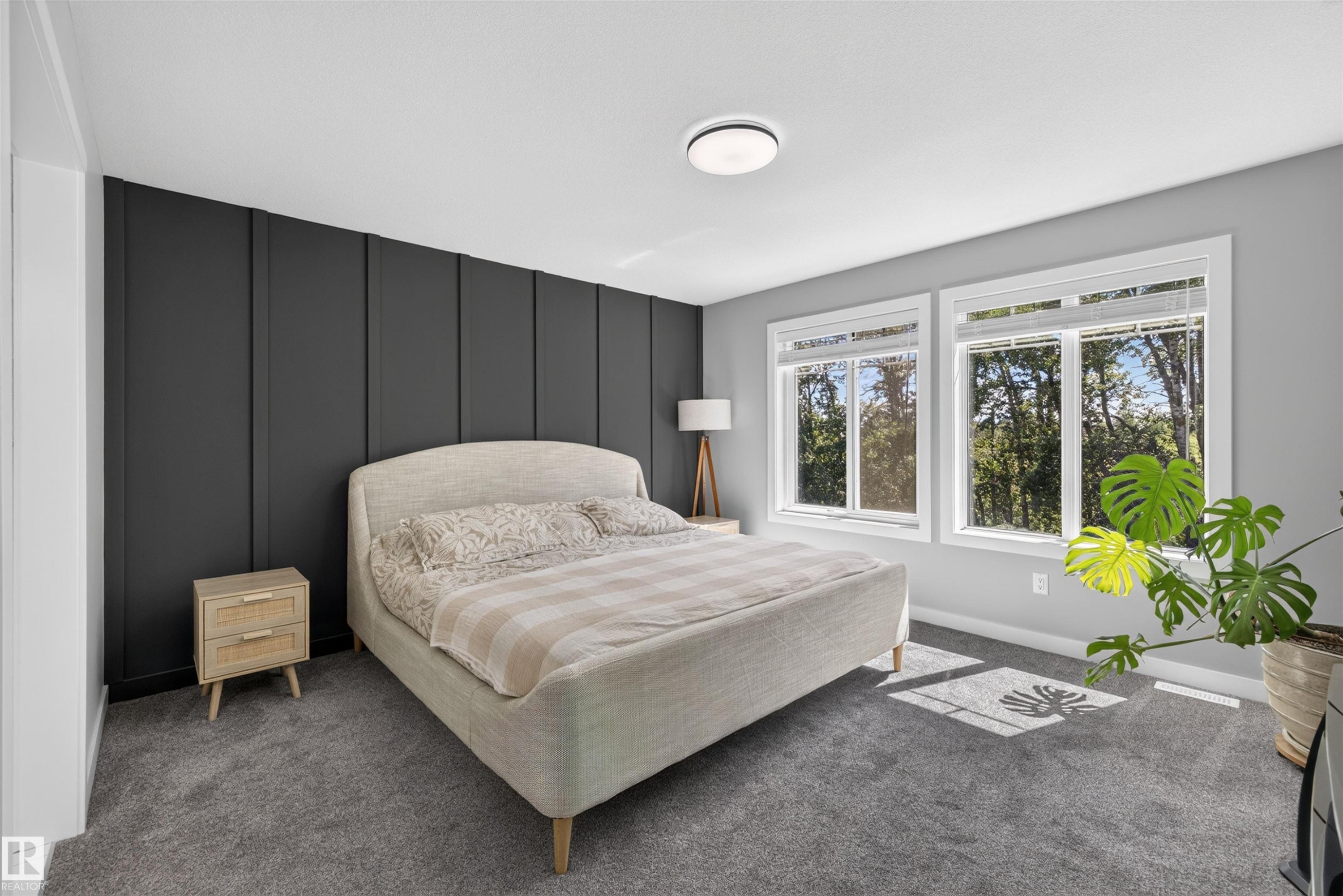 Bedroom featuring a dark paneled accent wall, two large windows with white trim, gray wall paint, gray carpeting, and a flush-mount ceiling light - 1573 Esaiw Place Nw, Edmonton, AB