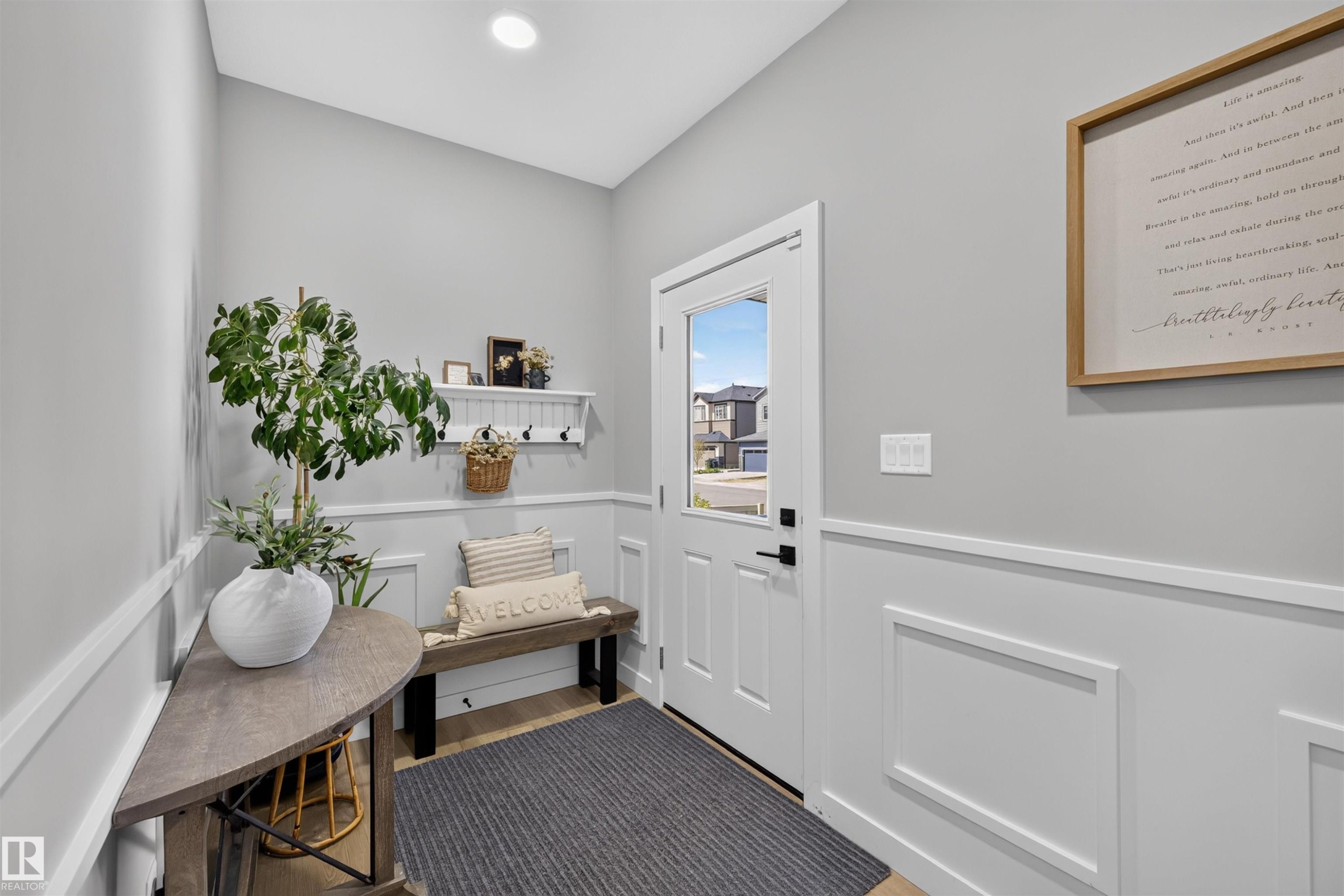 Entryway featuring paneled wainscoting, light wood-finish flooring, and a white front door with a clear glass insert - 1573 Esaiw Place Nw, Edmonton, AB