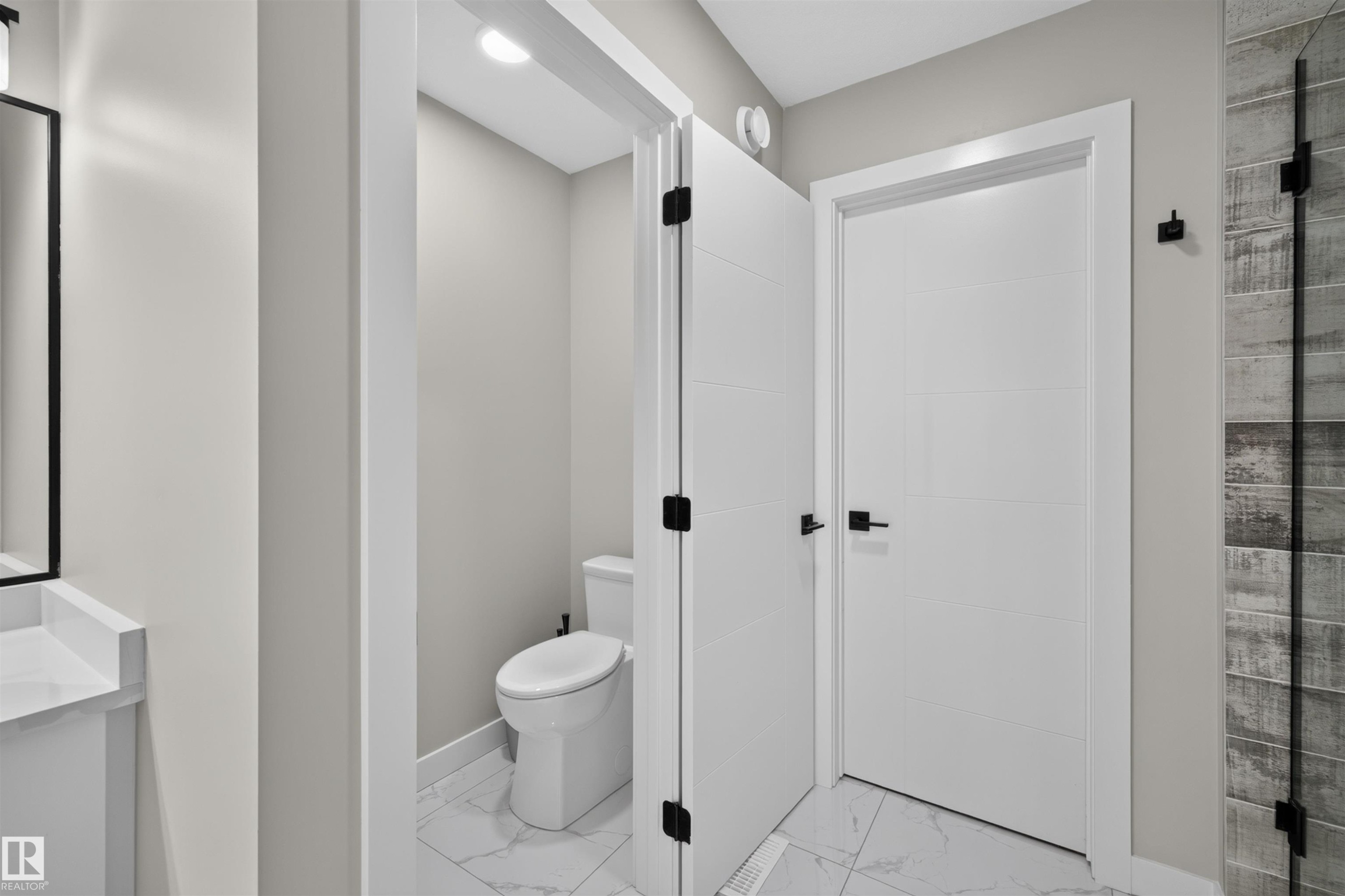 Modern bathroom featuring a toilet enclosure with marble-look tile flooring - 1573 Esaiw Place Nw, Edmonton, AB