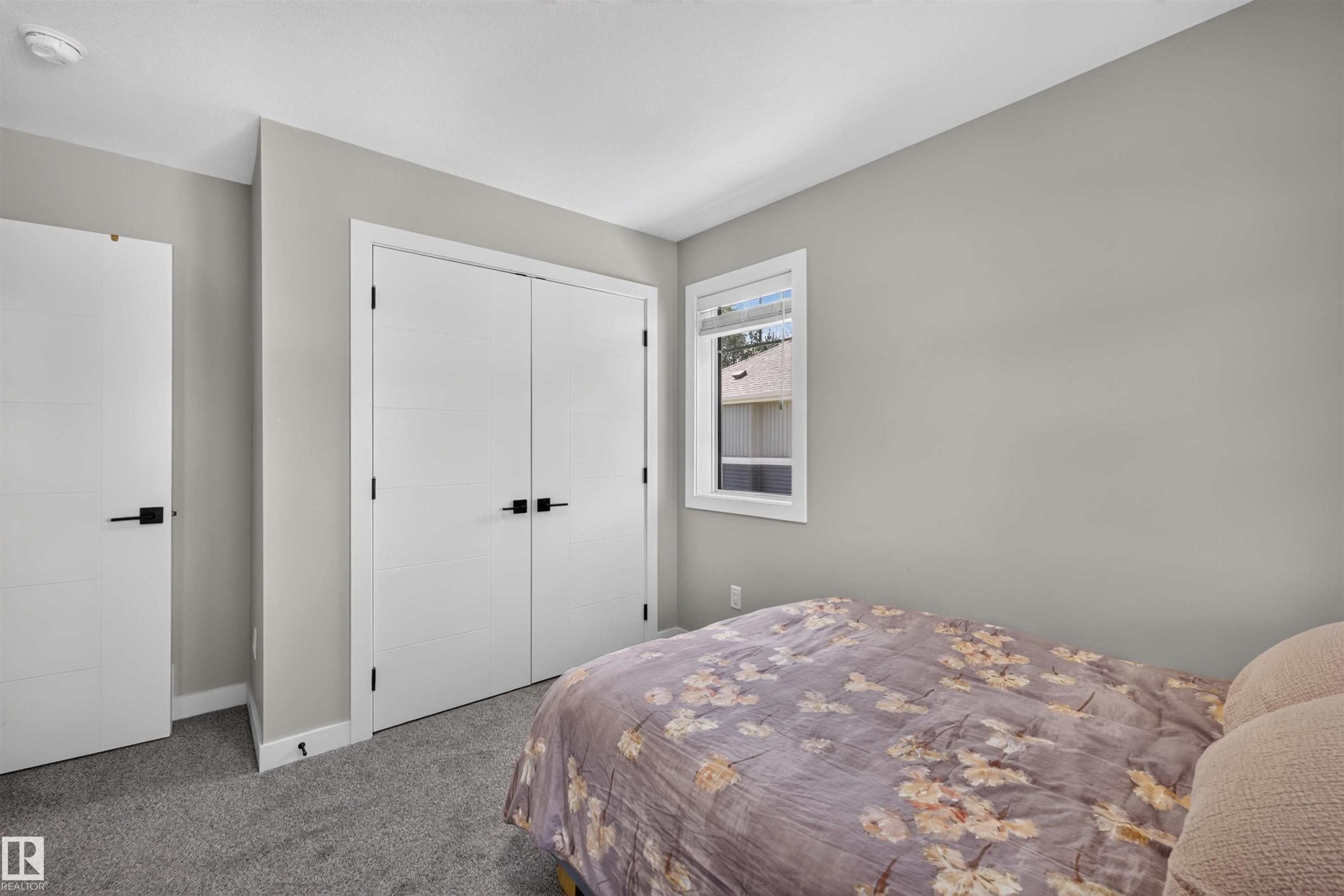 Neutral-toned room featuring a single window, white trim, gray carpet, and two white doors with black hardware - 1573 Esaiw Place Nw, Edmonton, AB