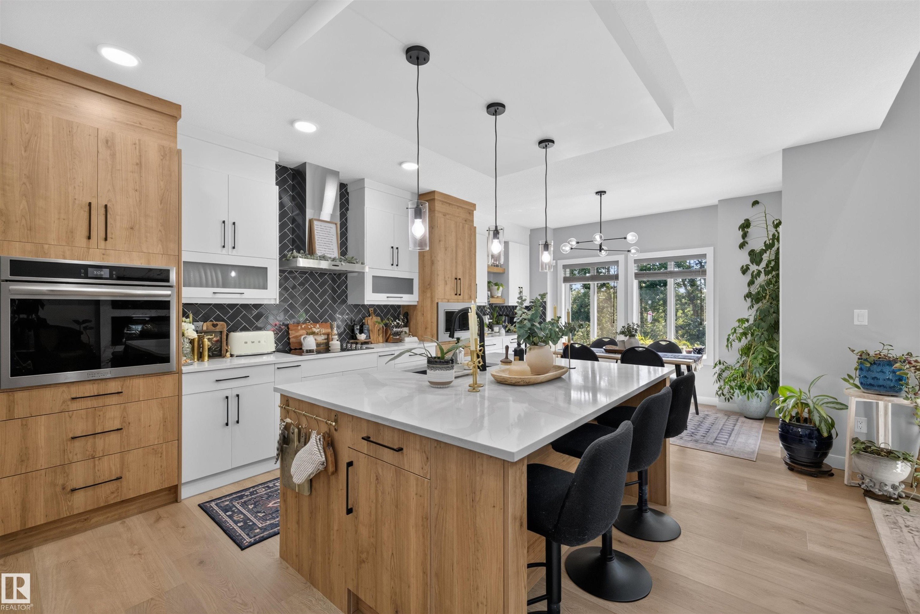 Modern kitchen featuring a large central island with seating, integrated oven, herringbone tile backsplash, and light wood-finish flooring - 1573 Esaiw Place Nw, Edmonton, AB