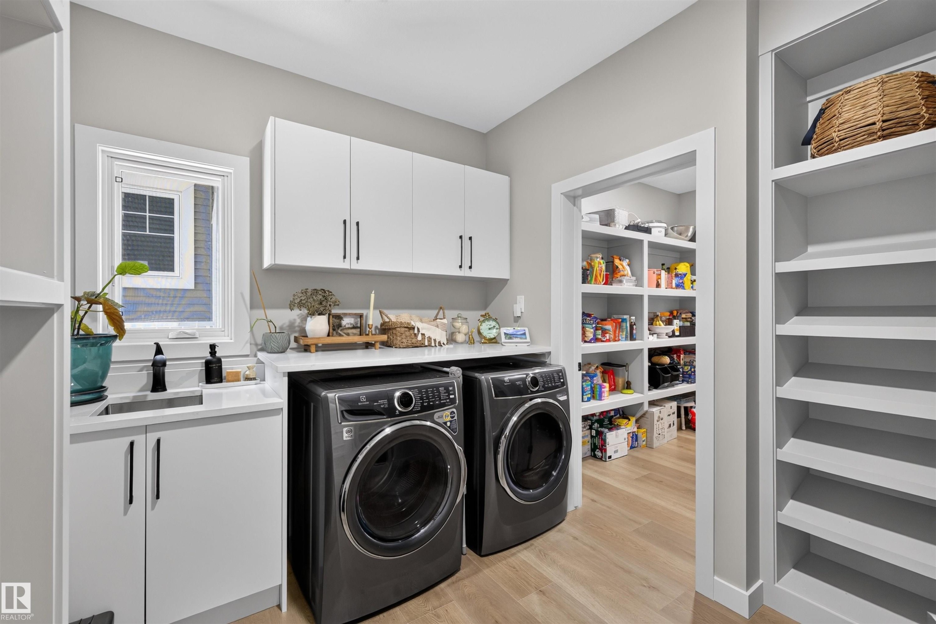 Dedicated utility room featuring light wood-finish flooring, white cabinetry with dark hardware, a countertop with an inset sink, and built-in shelving - 1573 Esaiw Place Nw, Edmonton, AB