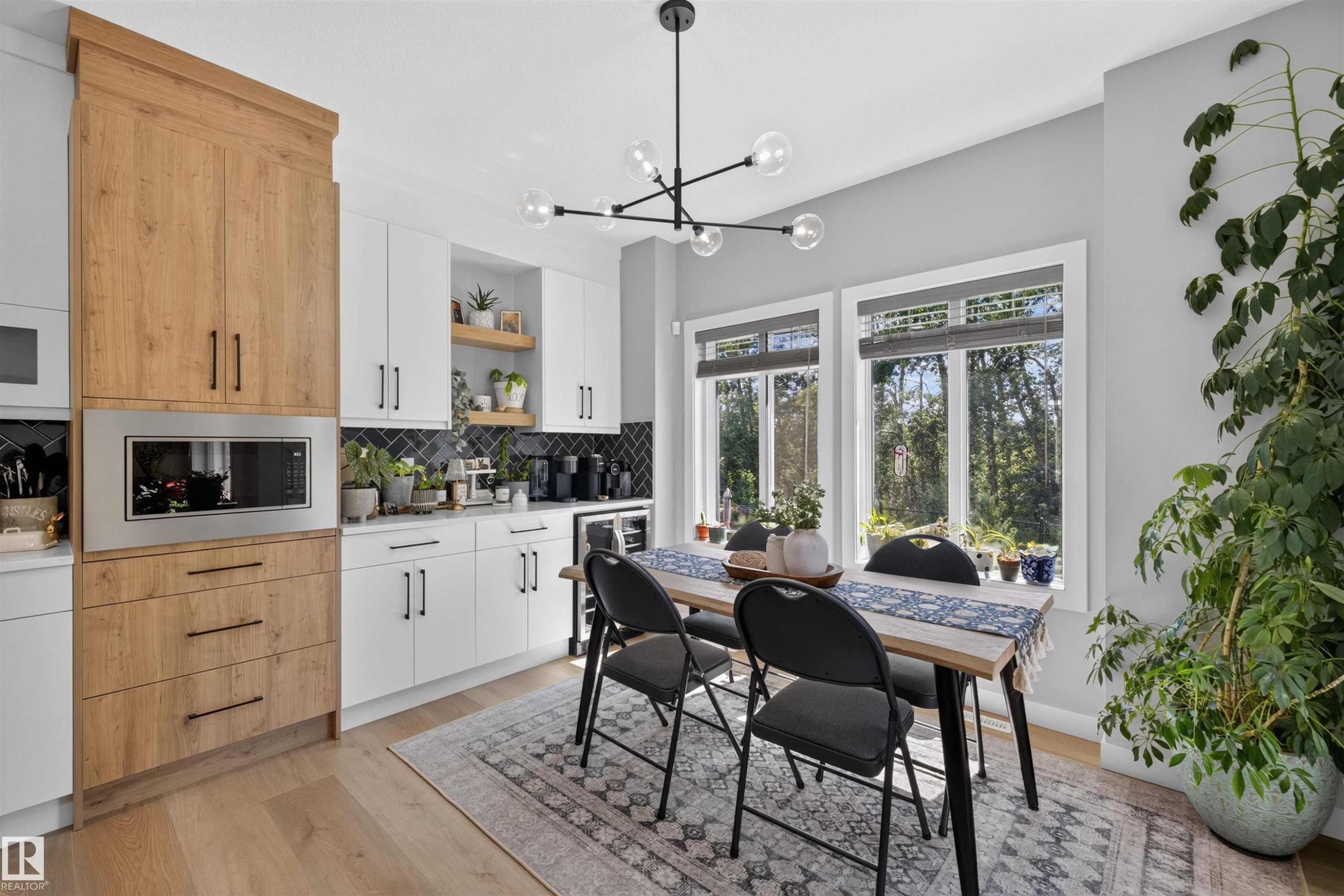 Modern kitchen and dining area featuring white shaker-style cabinetry with matte black hardware, a built-in microwave, wood-finish flooring, and a black geometric chandelier - 1573 Esaiw Place Nw, Edmonton, AB