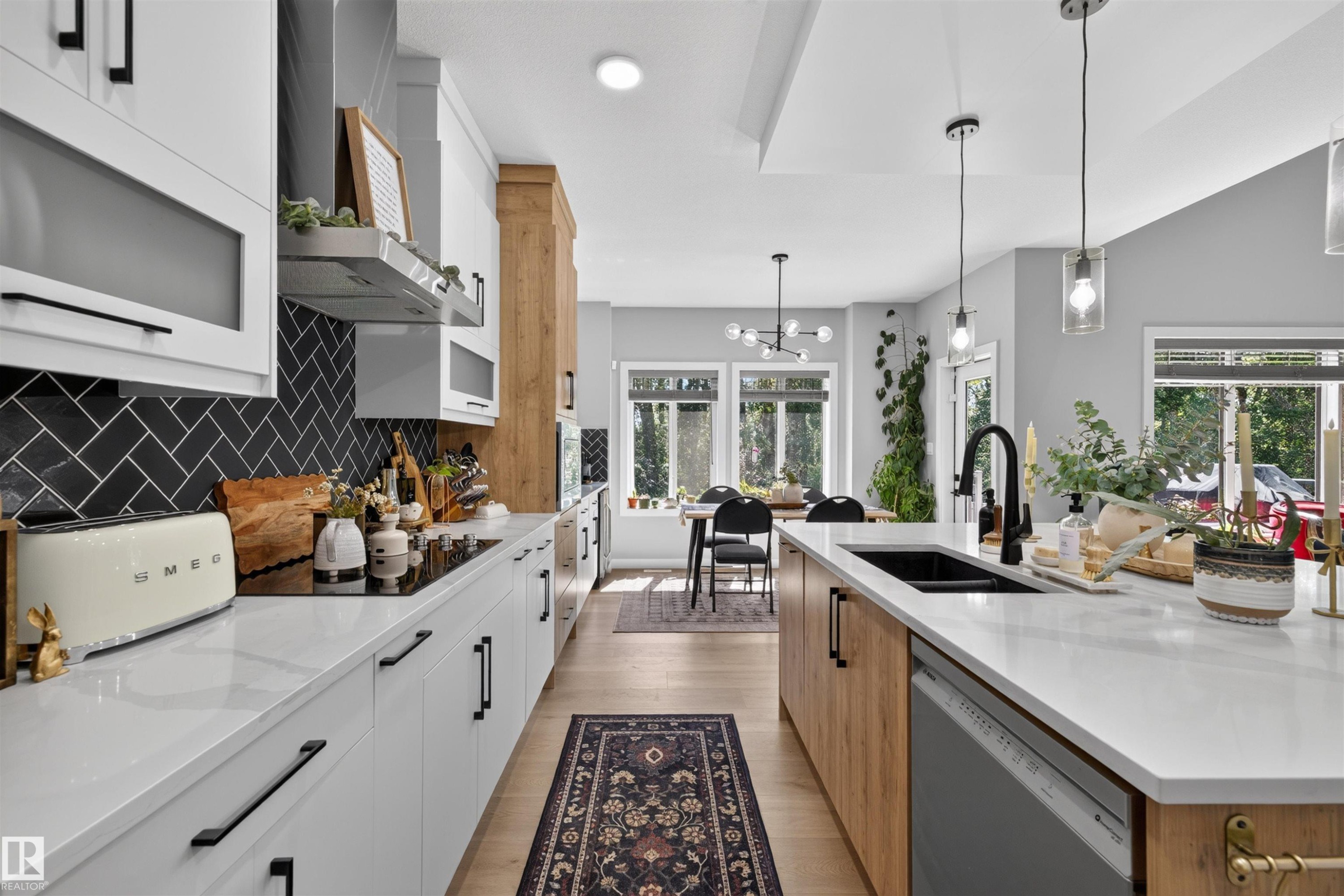 Modern kitchen featuring light wood-finish flooring, white cabinetry with black hardware, and a black herringbone tile backsplash - 1573 Esaiw Place Nw, Edmonton, AB