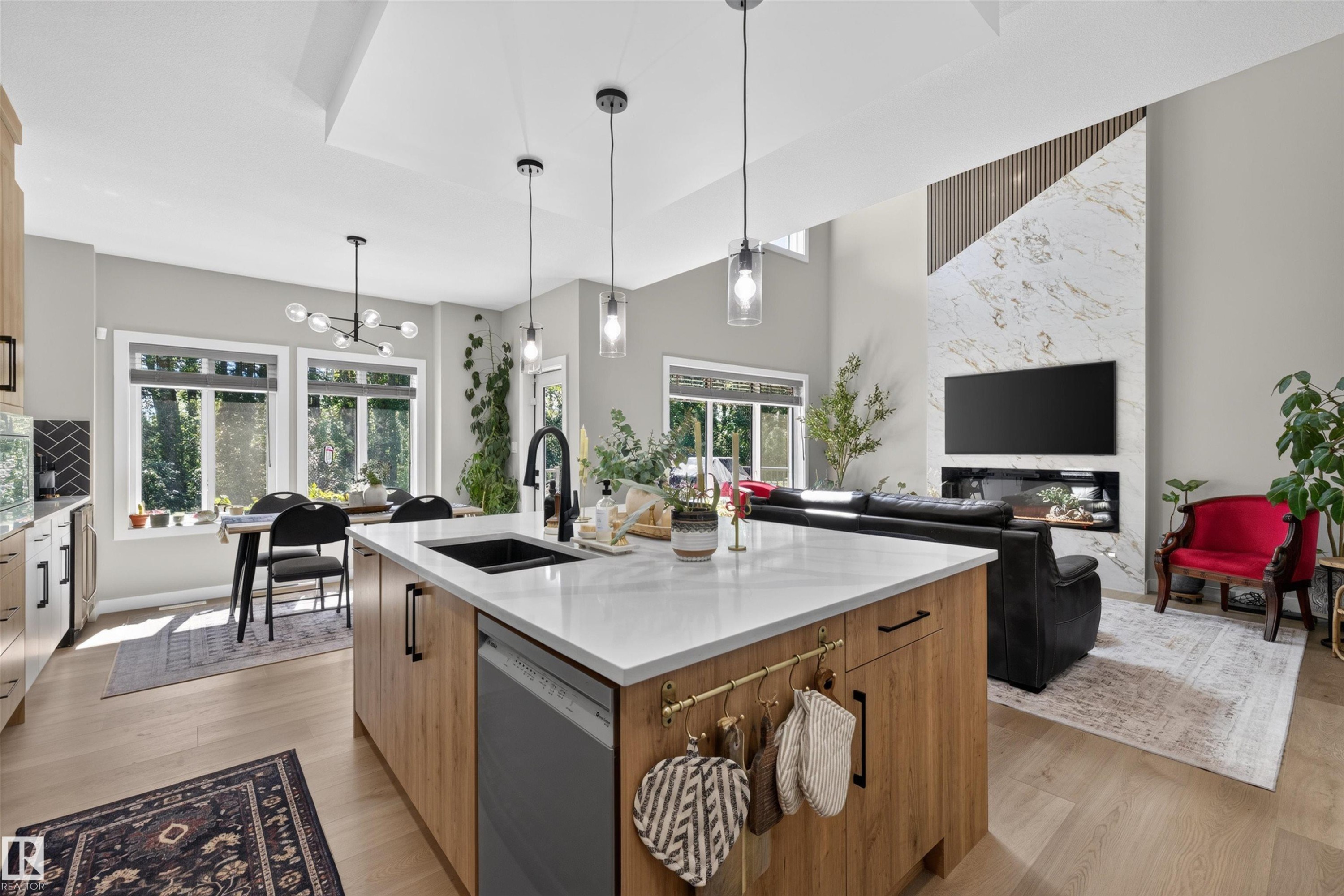 Open-concept kitchen and living area featuring a large center island with a built-in sink, wood-finish flooring, and pendant lighting - 1573 Esaiw Place Nw, Edmonton, AB